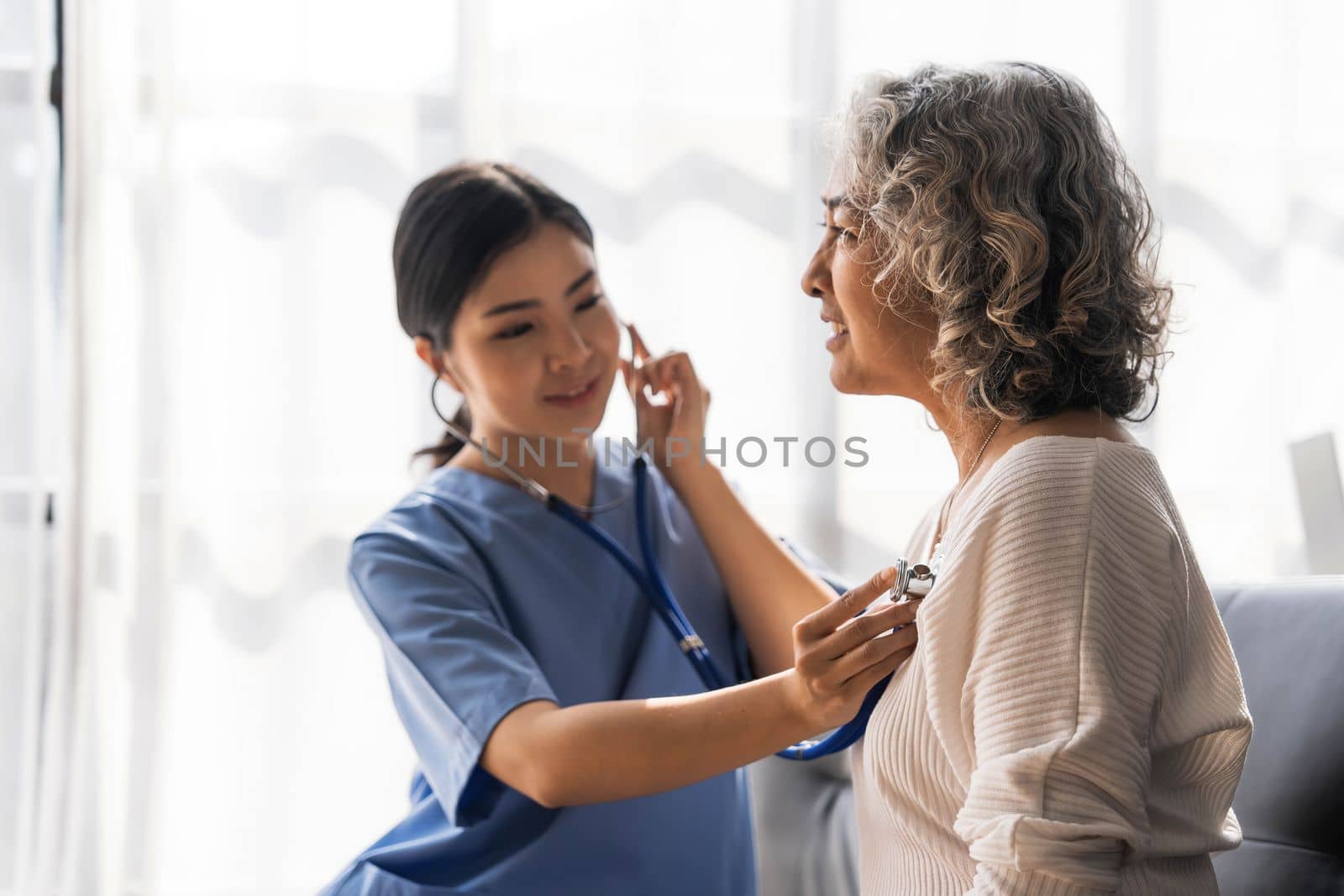 Stethoscope exam. Attractive cheerful asian female doctor listening to the elderly while using stethoscope by wichayada