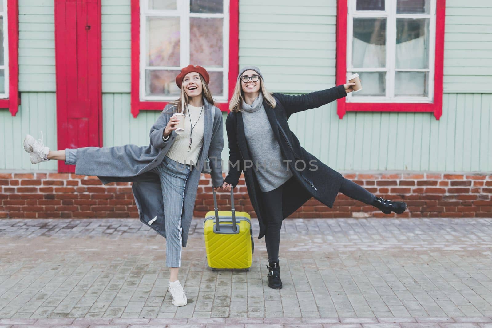 Two cheerful funny tourist women smiling and fool around and with suitcases on city street in autumn or spring time - travel and vacation concept by Satura86