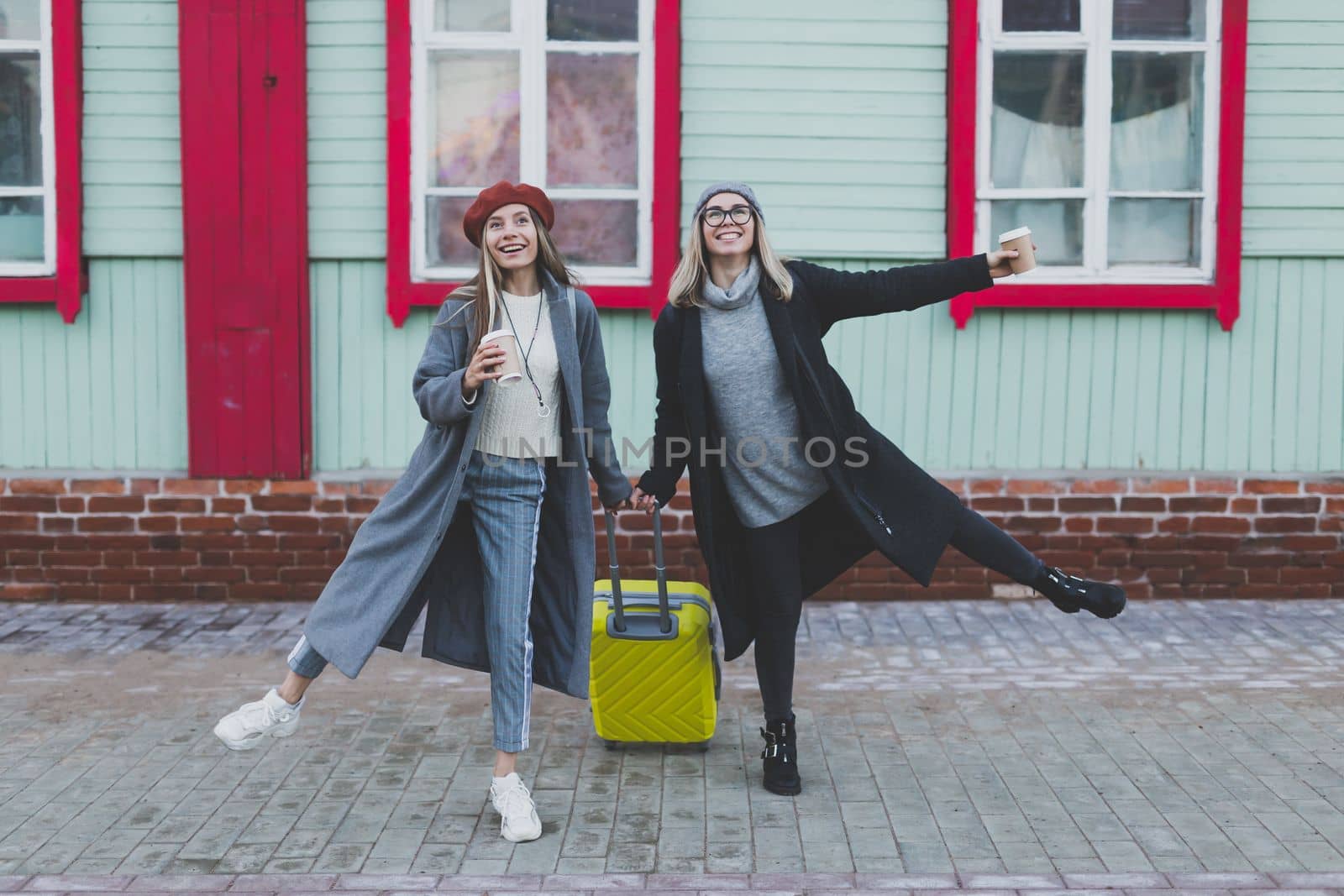 Two cheerful funny tourist women smiling and fool around and with suitcases on city street in autumn or spring time - travel and vacation concept by Satura86