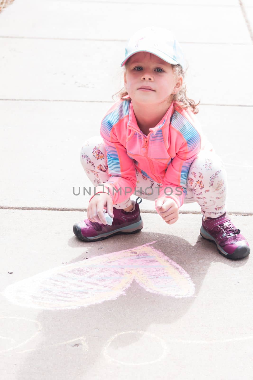 Little girl playing with chalk on a driveway in front of the house.
