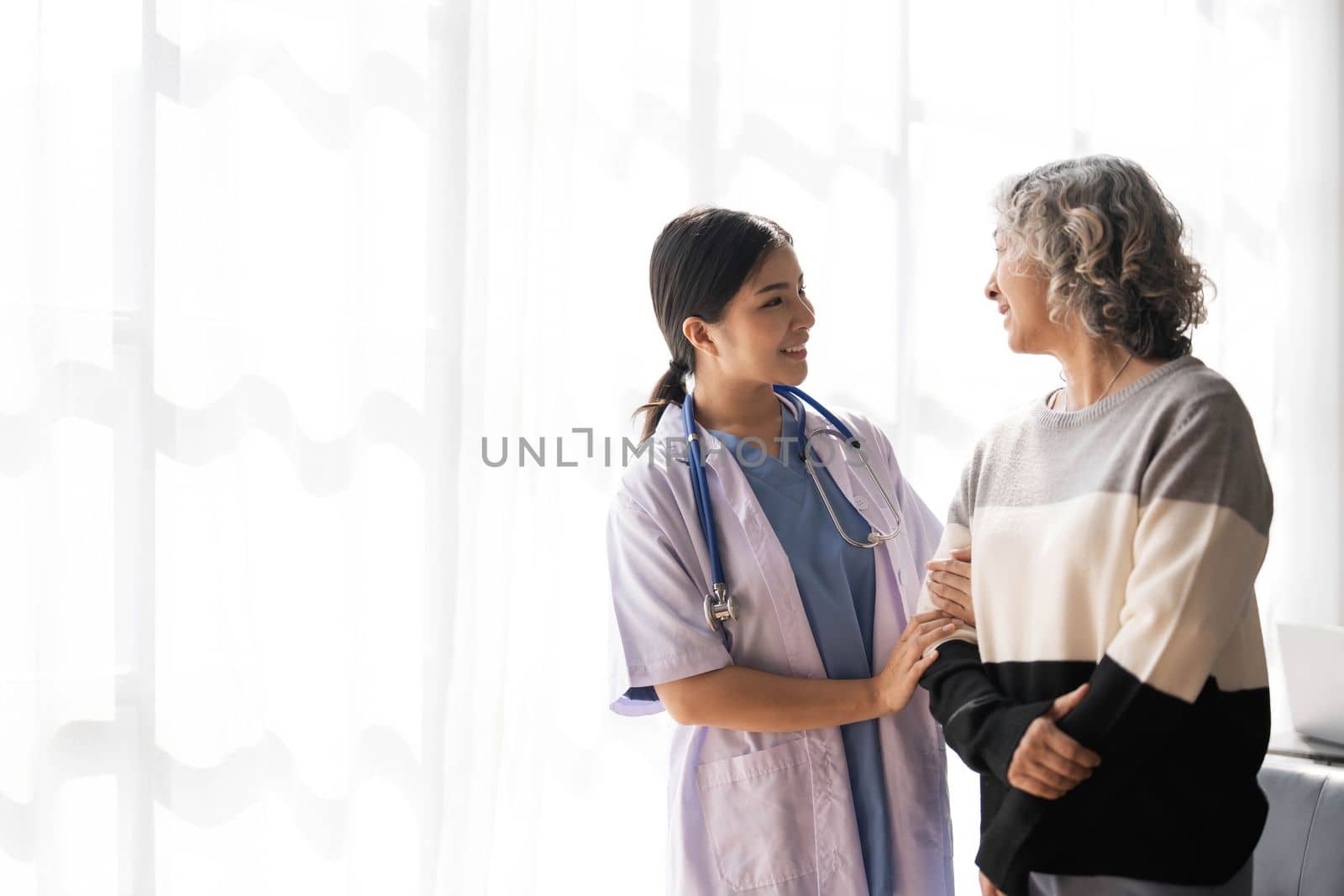 Young caregiver helping senior woman walking. Nurse assisting her old woman patient at nursing home. Senior woman with walking stick being helped by nurse at home...