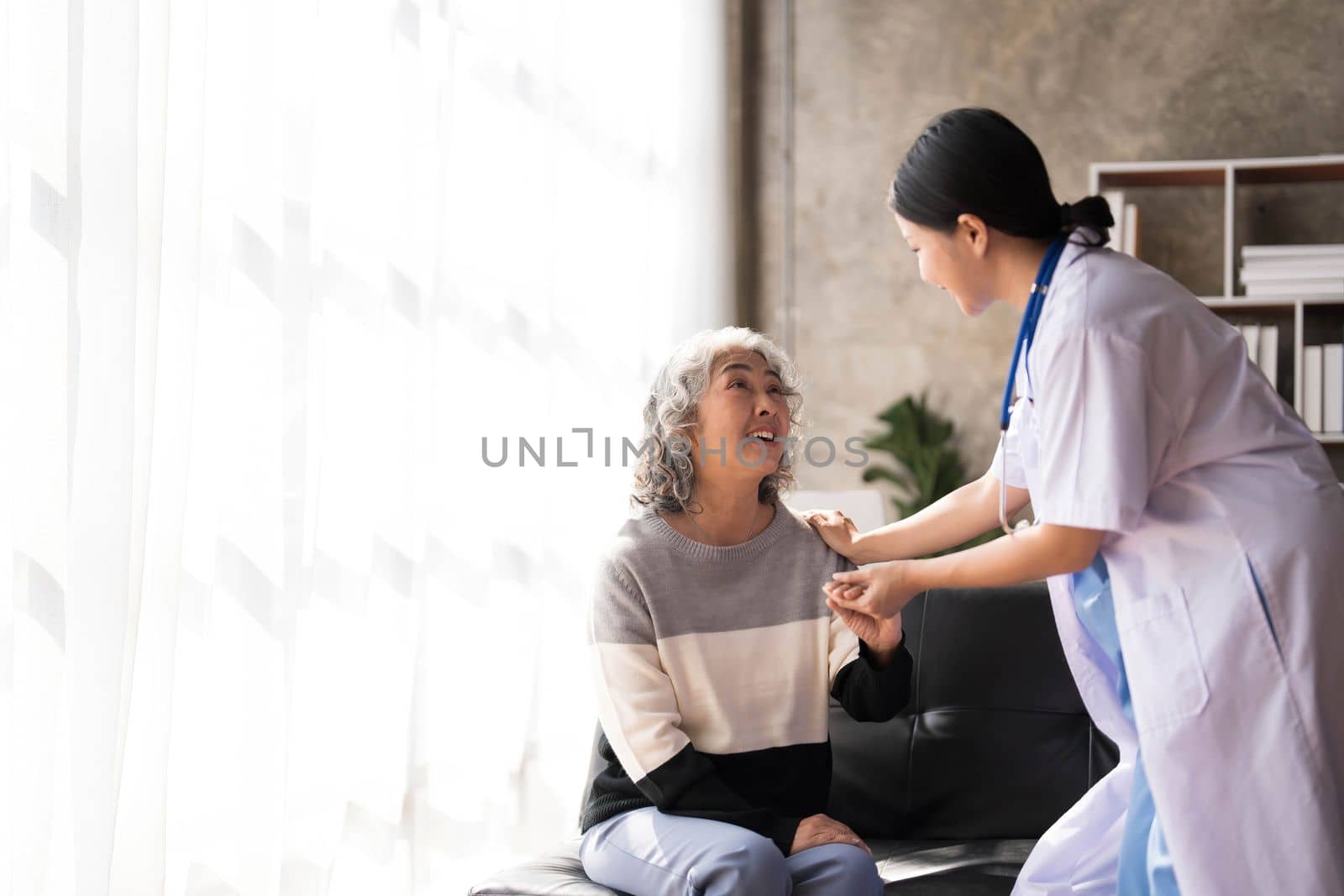 Young caregiver helping senior woman walking. Nurse assisting her old woman patient at nursing home. Senior woman with walking stick being helped by nurse at home. by wichayada