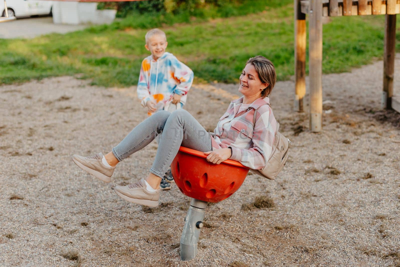 Mother and son having fun on a swing. Motherhood and childhood concept. Sunny summer day. Beautiful family is having fun outside. Parents with children riding on a swing. Mom is playing with her little son on a terrace with swings. A mother woman swings on a swing in the park. Mom and child are on a swing in nature by Andrii_Ko