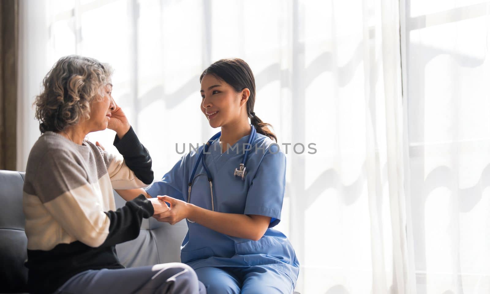 Young caregiver helping senior woman walking. Nurse assisting her old woman patient at nursing home. Senior woman with walking stick being helped by nurse at home. by wichayada
