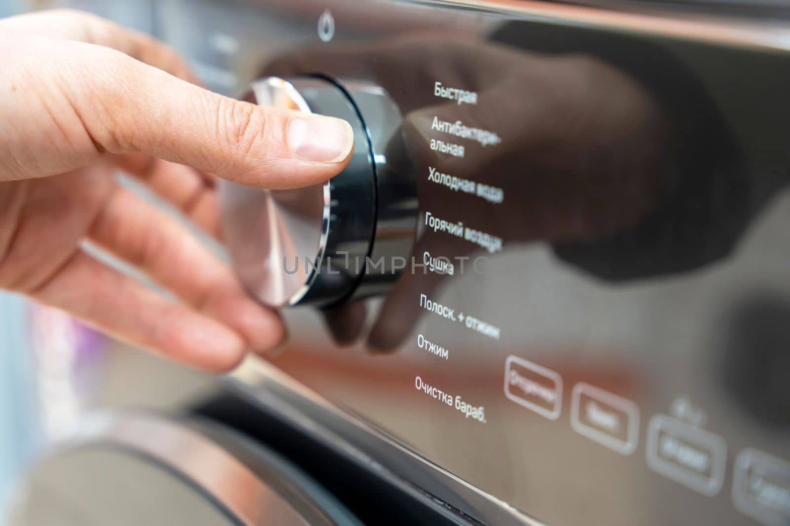 a woman's hand selects the washing mode with a round selector on the control panel of a modern washing machine. technologies. close-up. choosing a washing program