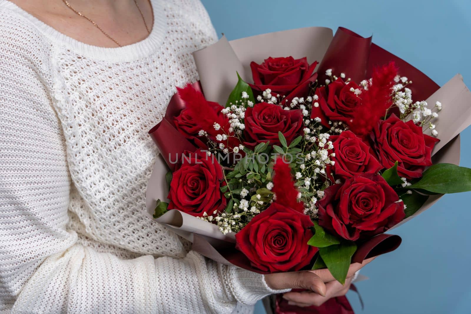 a beautiful bouquet of fresh red roses in women's hands on a light blue background. Congratulations on Mother's Day. valentine's day. wedding