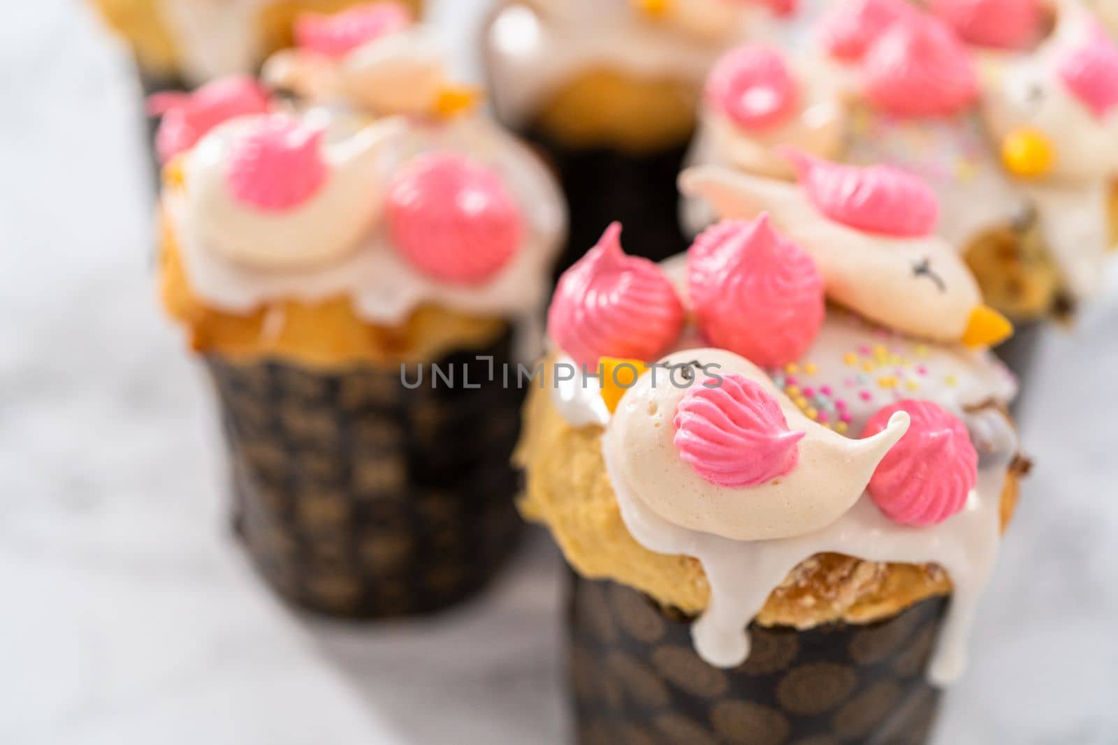 Freshly baked mini Easter bread kulich with lemon glaze, decorated with sprinkles and meringue bird-shaped cookies.