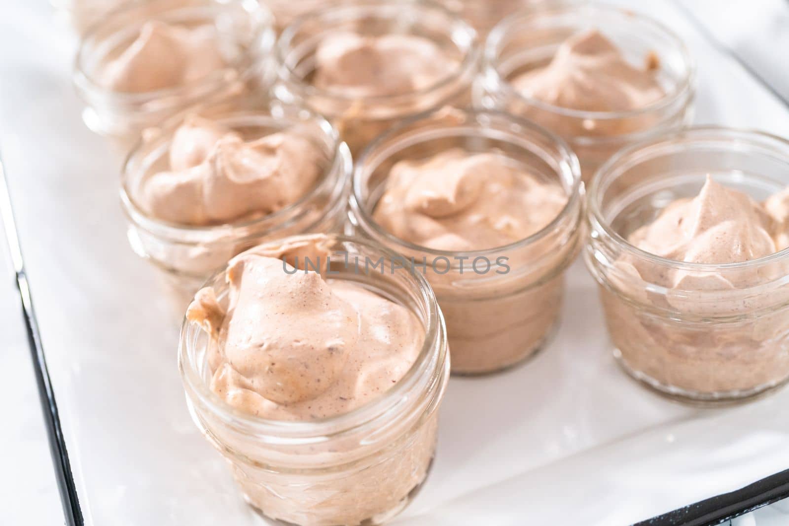 Scooping mixture into the small glass jars to make homemade chocolate ice cream.