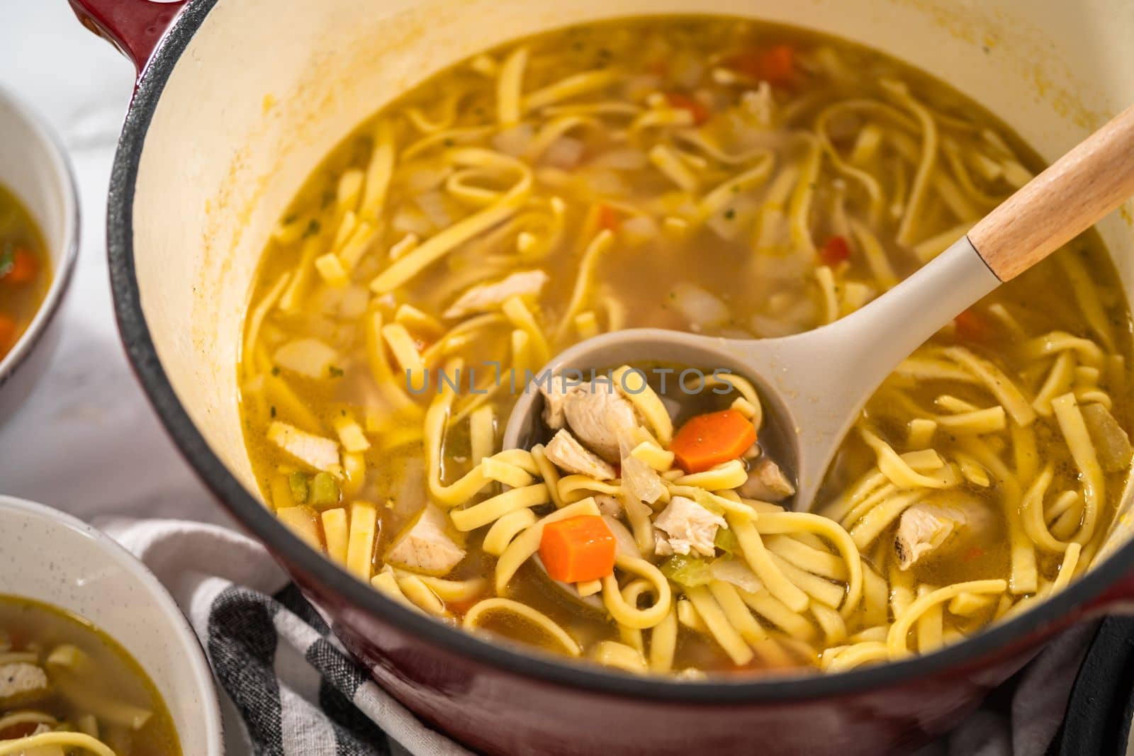 Serving chicken noodle soup with kluski noodles in white ceramic soup bowls.