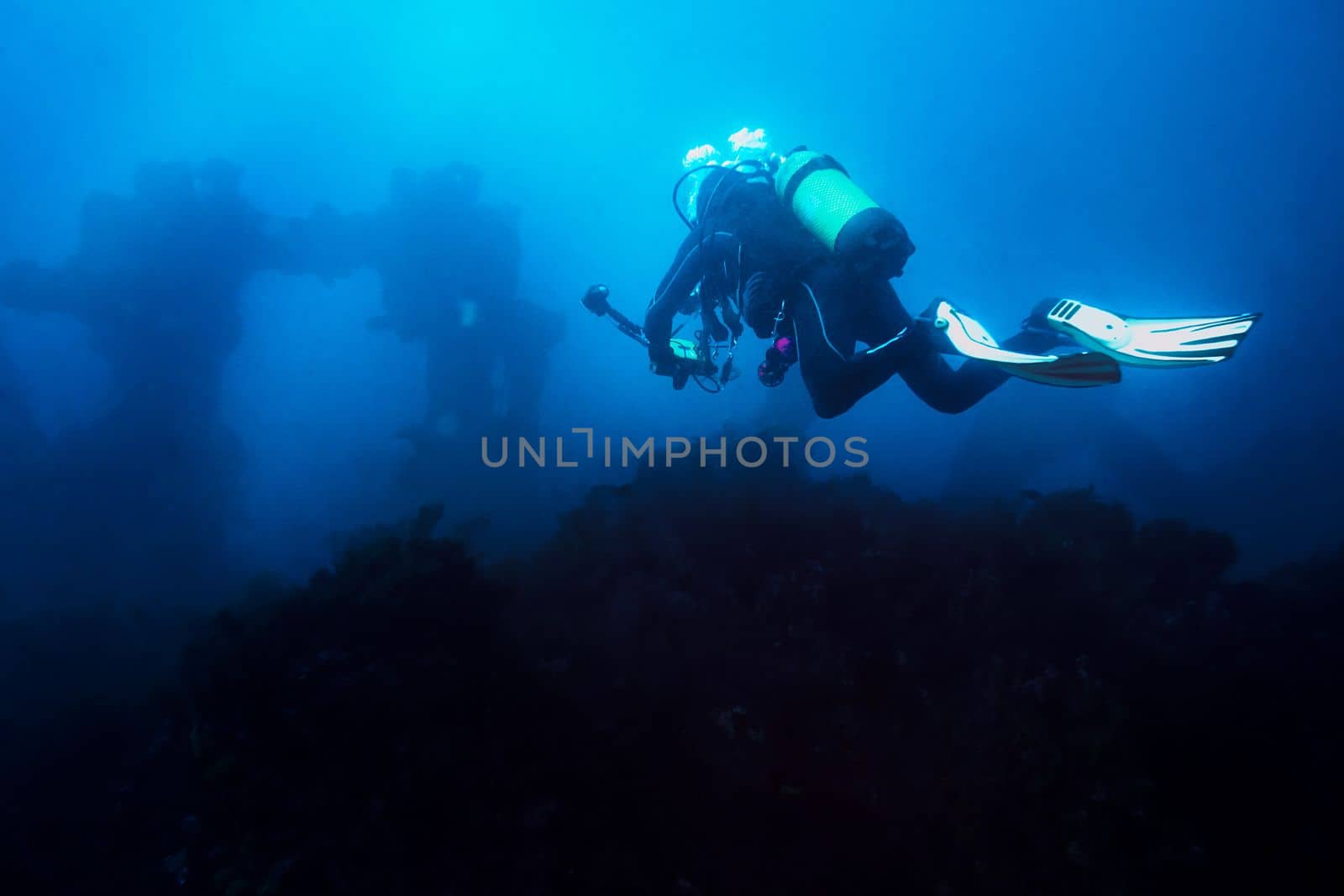 diver with his camera taking a dive through the blue sea towards the wreck. The old remains of the ship look distant and blurred giving an aura of mystery