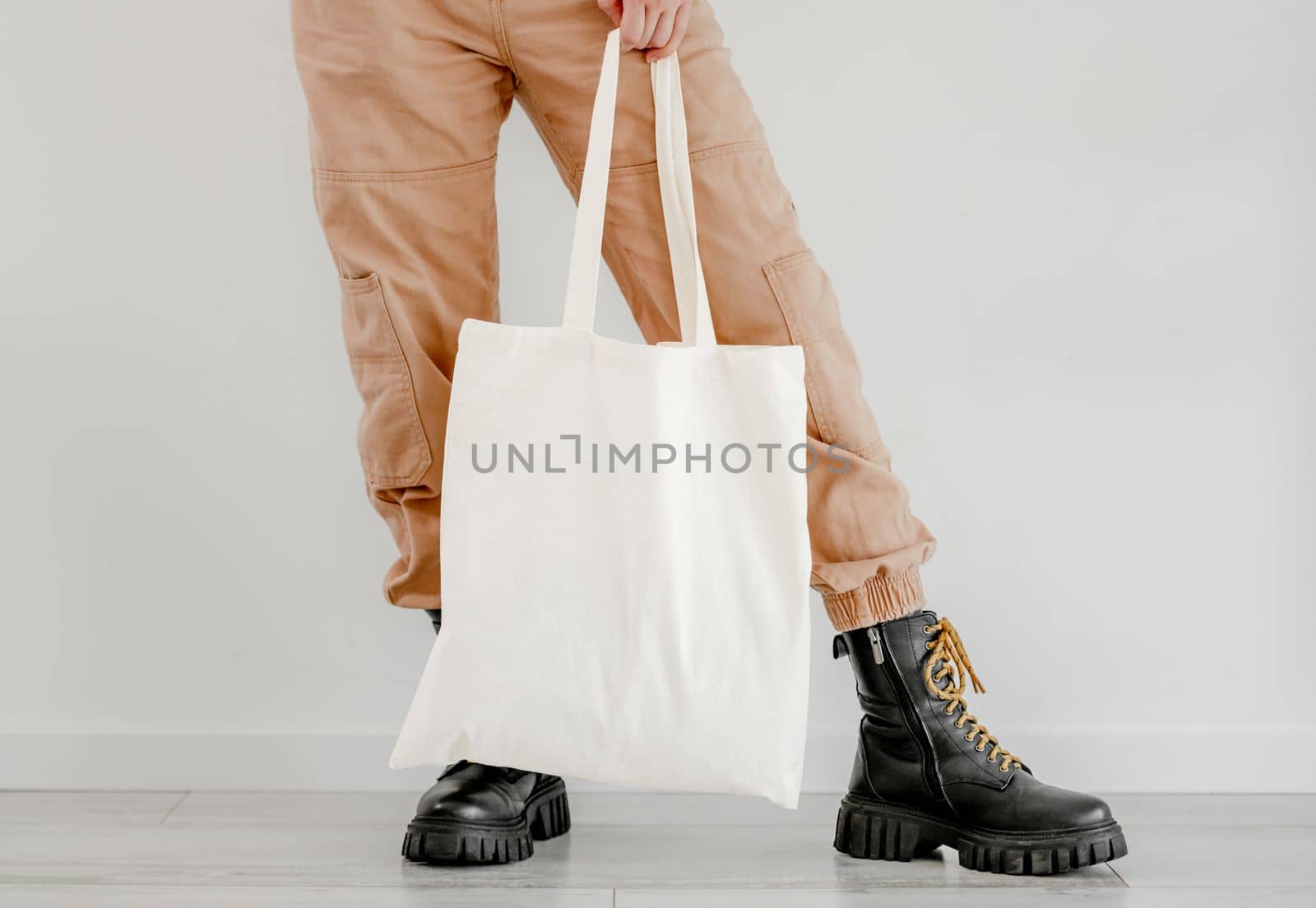 Girl in boots and pants holding cotton linen eco bag mockup. Woman legs with environment friendly shopping handbag with empty copy space for business