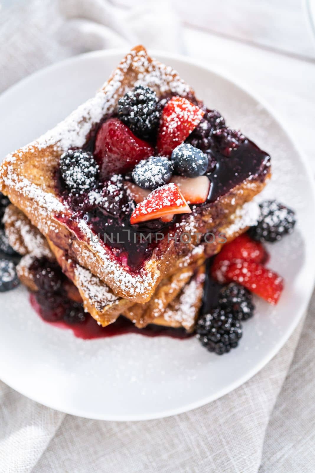 Stack of freshly made french toast garnished with mix berry compote and powder sugar.