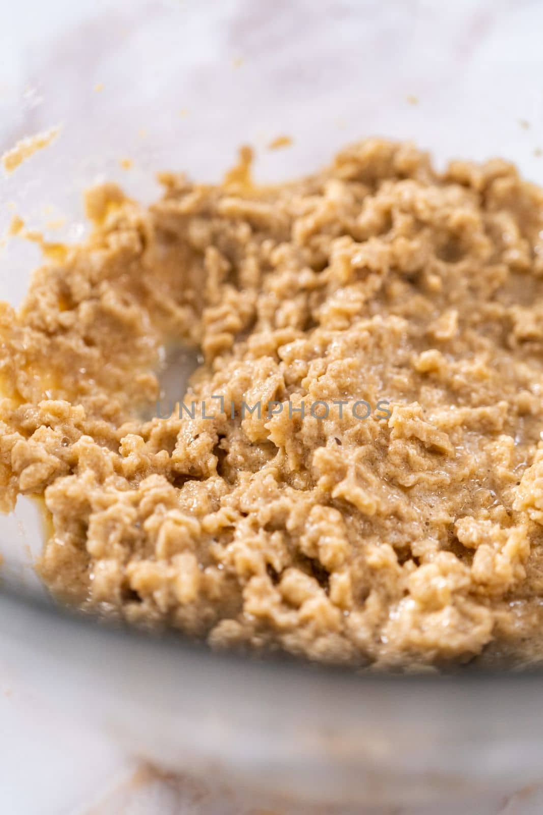 Mixing ingredients in a large glass mixing bowl to bake apple oatmeal cookies.