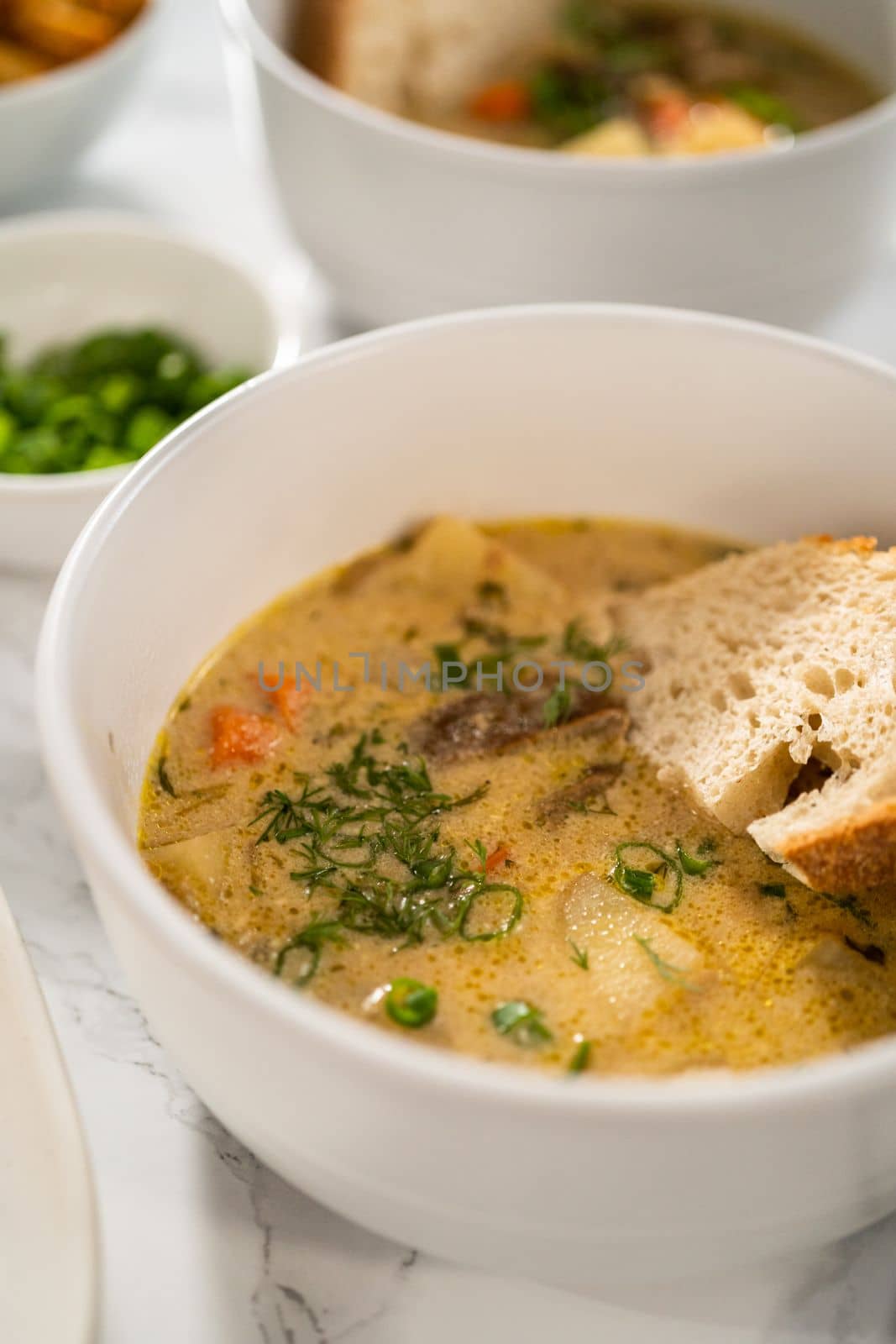 Serving creamy wild mushroom soup made out of dehydrated wild mushrooms in white bowls with sourdough bread.