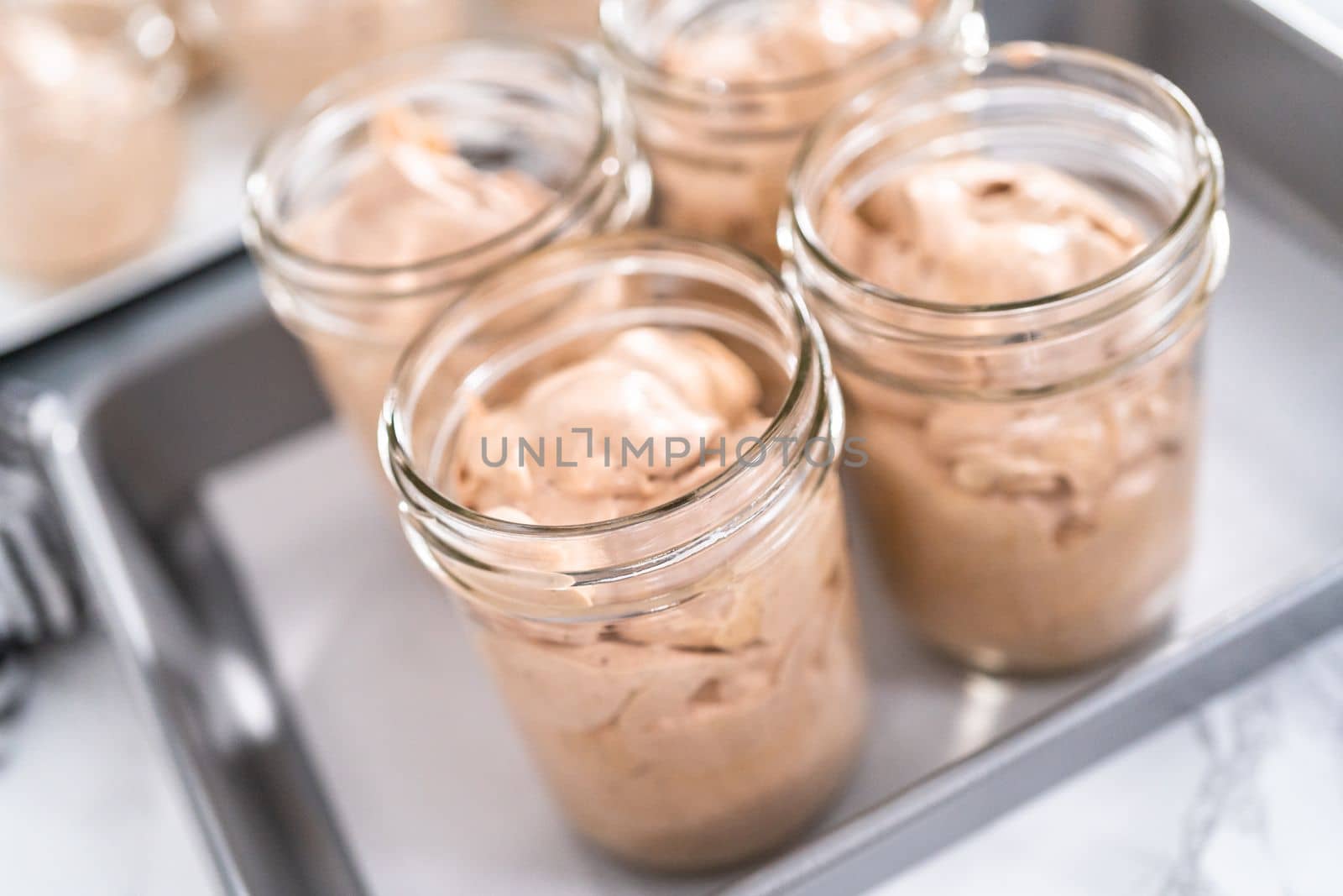 Scooping mixture into the small glass jars to make homemade chocolate ice cream.