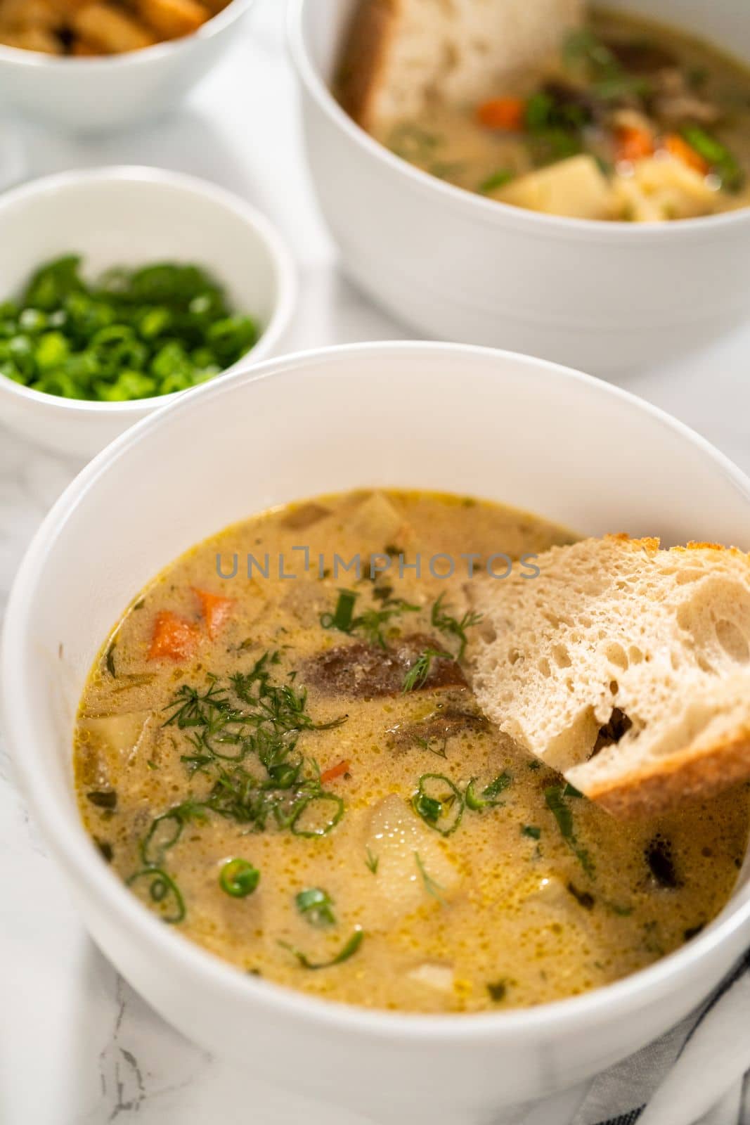Serving creamy wild mushroom soup made out of dehydrated wild mushrooms in white bowls with sourdough bread.