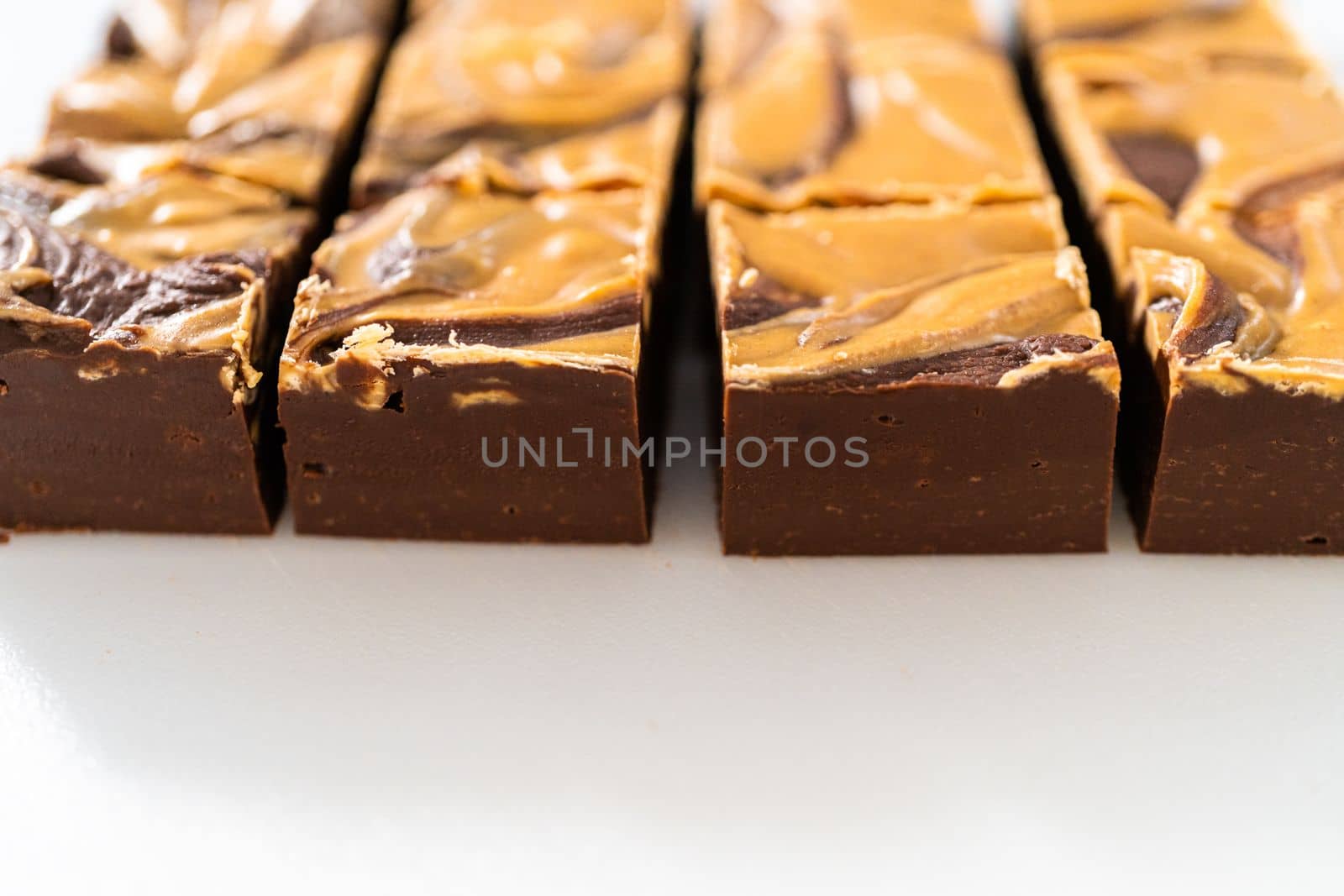 Cutting chocolate fudge with peanut butter swirl into small pieces on a white cutting board.