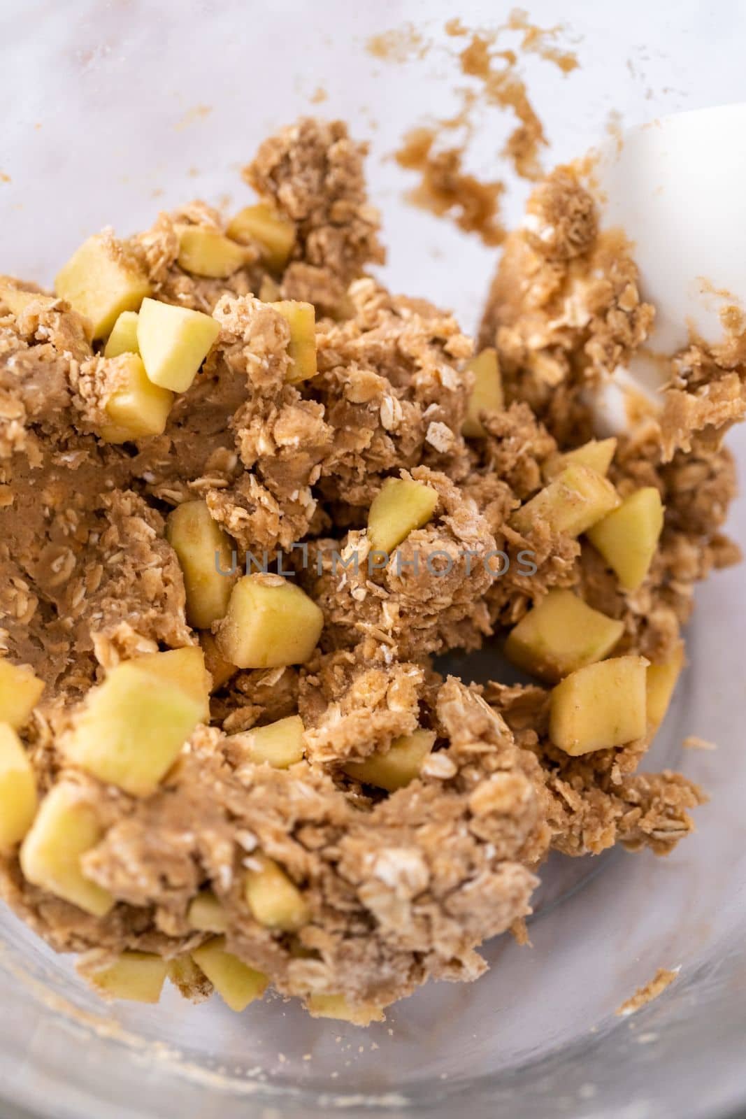 Mixing ingredients in a large glass mixing bowl to bake apple oatmeal cookies.