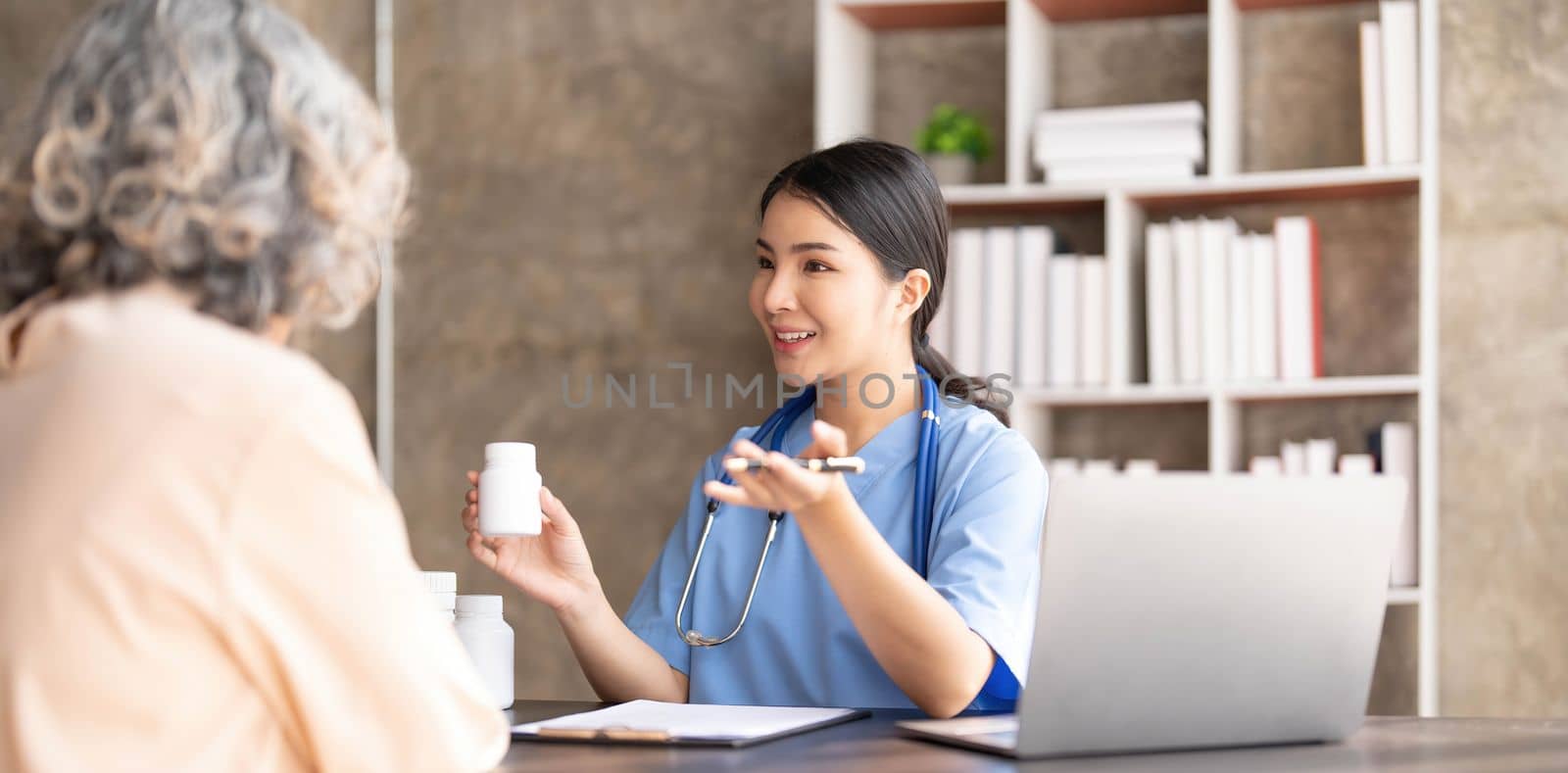 Asian Senior elderly female patient consult with physician nurse at nursing home care. Caregiver therapist pharmacist girl hold medicine pills bottle, explain prescription to older disabled guy in house