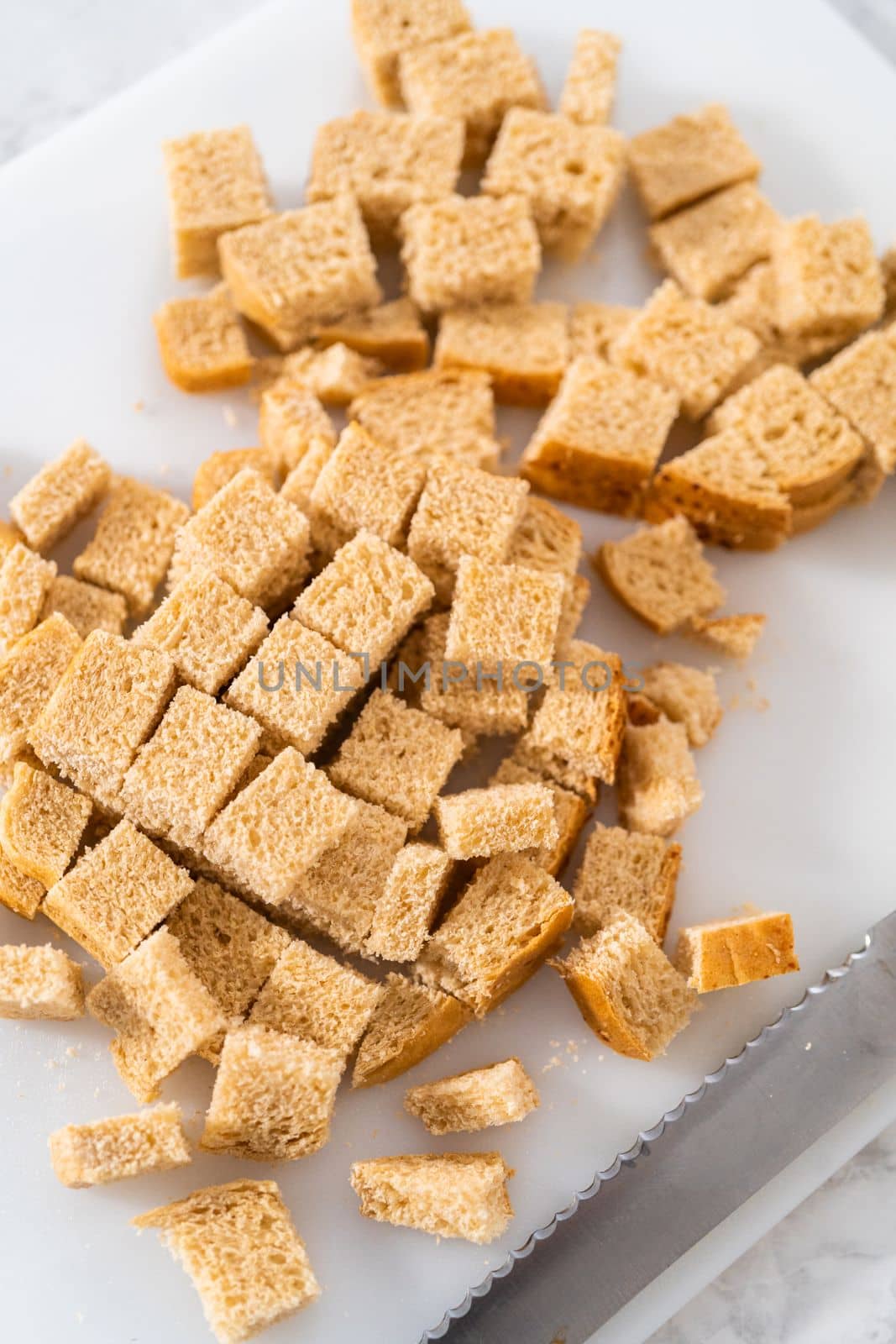 Cutting stale bread with a bread knife on a white cutting board to make croutons.