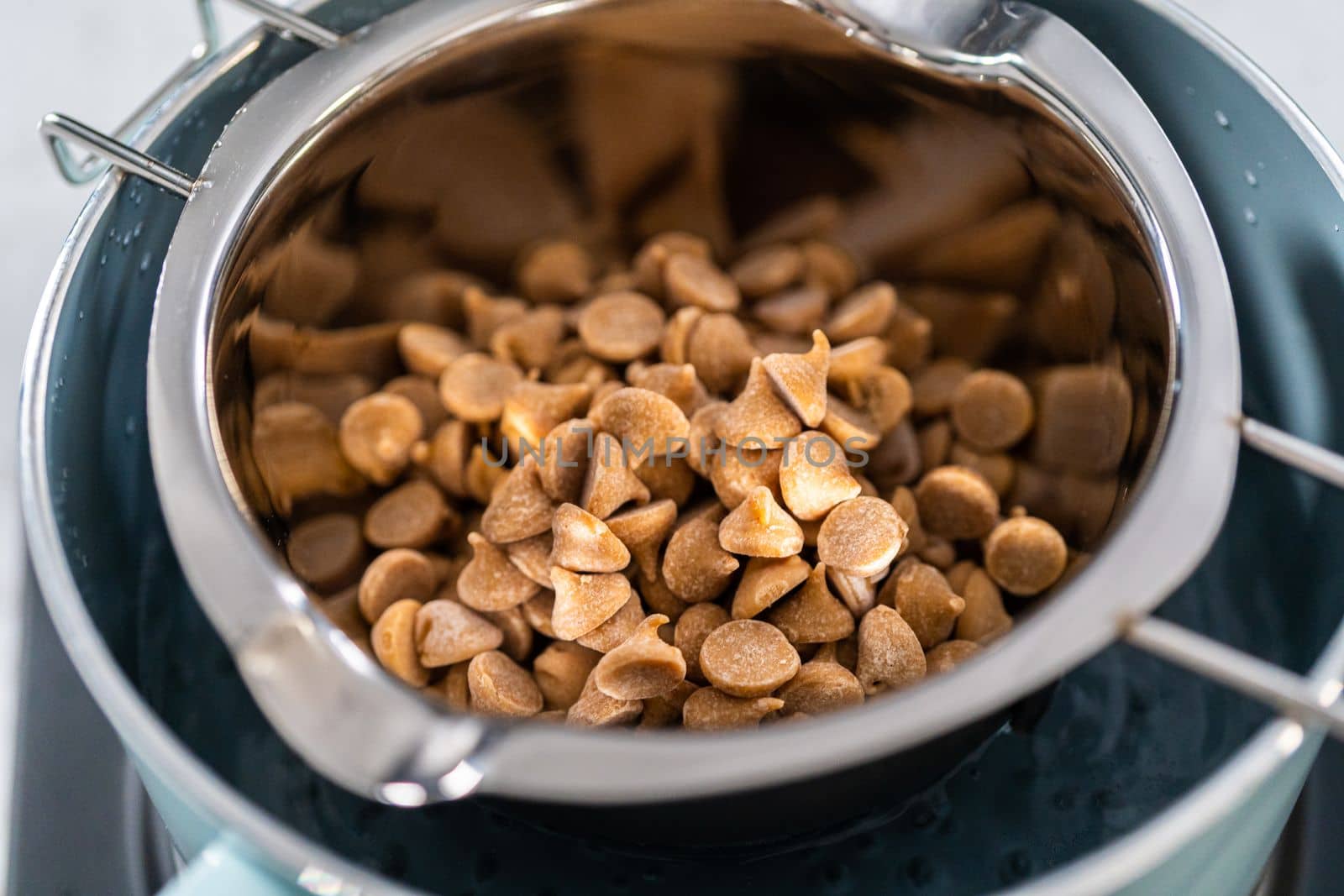 Melting chocolate chips and other ingredients in a glass mixing bowl over boiling water to prepare chocolate fudge with peanut butter swirl.