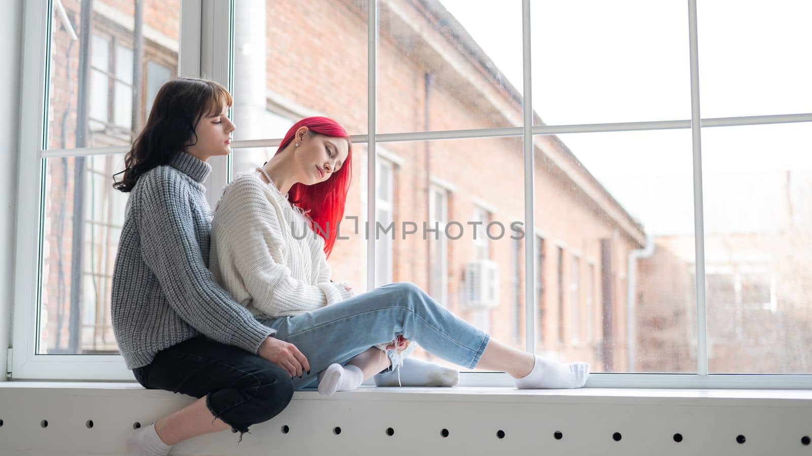 Two women dressed in sweaters sit by the window and gently hug. Lesbian intimacy