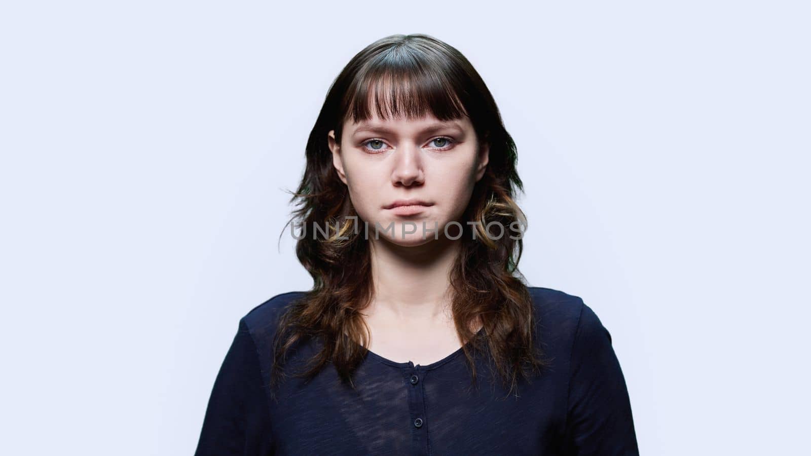 Headshot portrait of young confident female looking at camera on light background. Serious calm teenage girl 18, 19 years old. Lifestyle, emotion, face, youth, photo for documents, student travel card