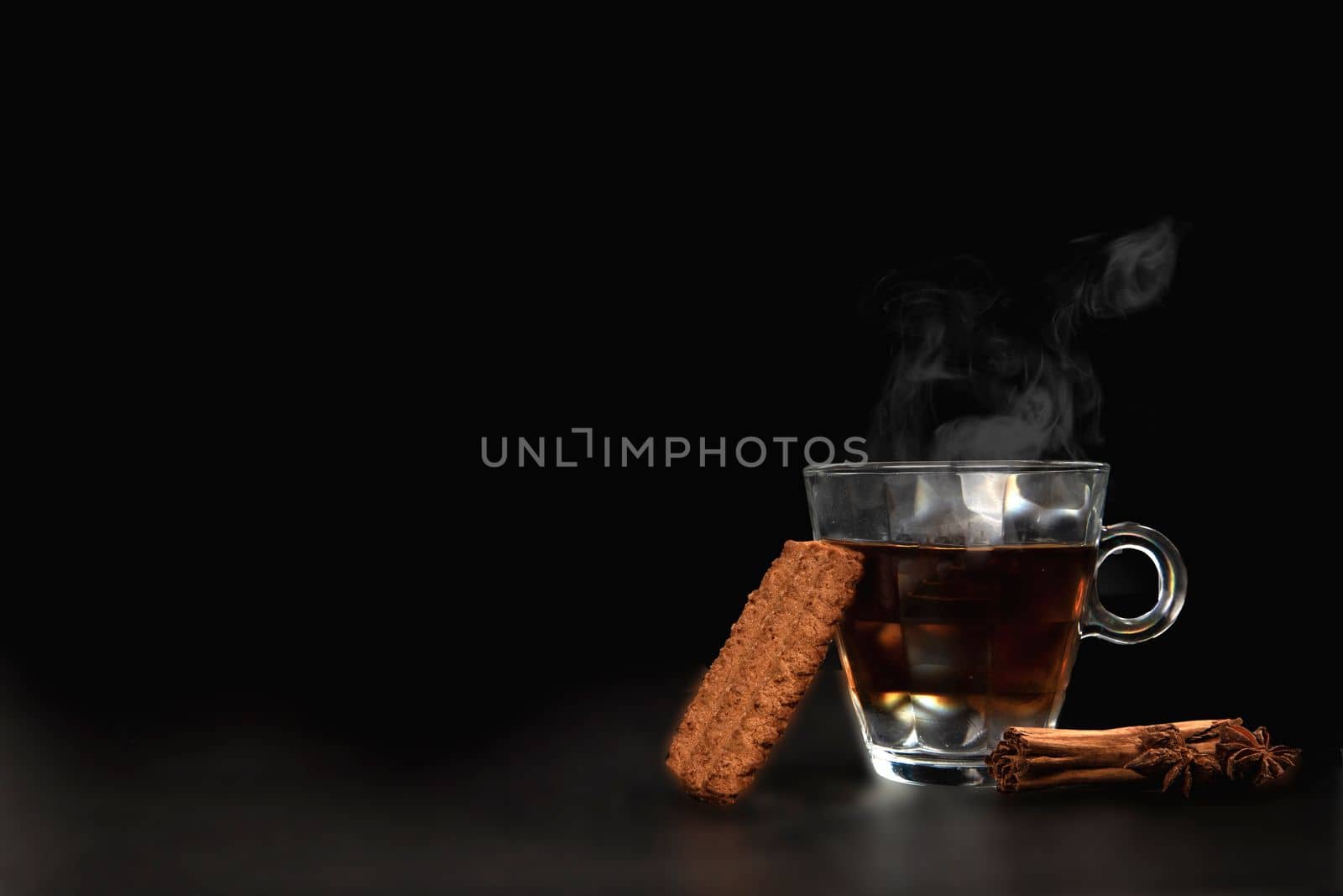 A glass of freshly brewed black tea,escaping steam,warm soft light, darker background. copy space healthy