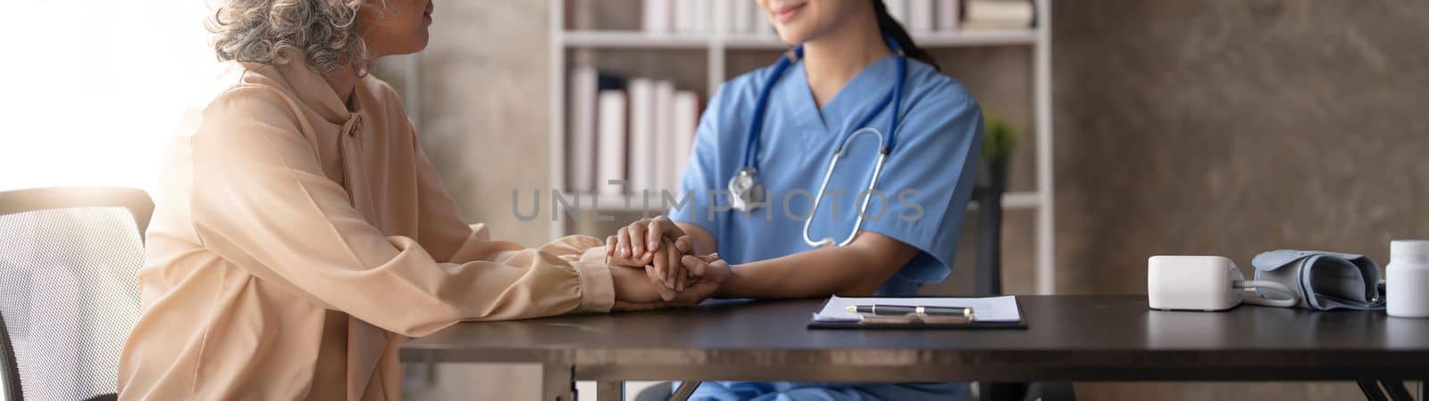 Happy patient is holding caregiver for a hand while spending time together. Elderly woman in nursing home and nurse..