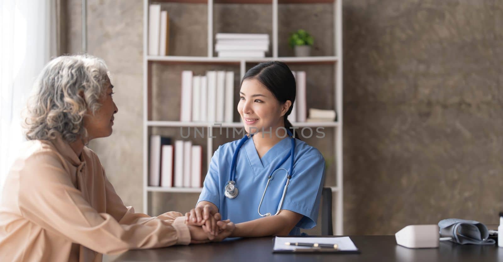 Happy patient is holding caregiver for a hand while spending time together. Elderly woman in nursing home and nurse..