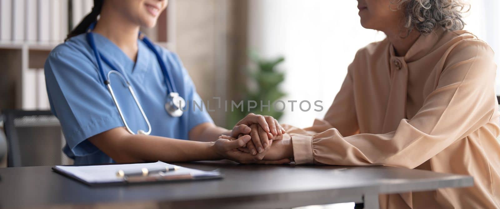 Happy patient is holding caregiver for a hand while spending time together. Elderly woman in nursing home and nurse..