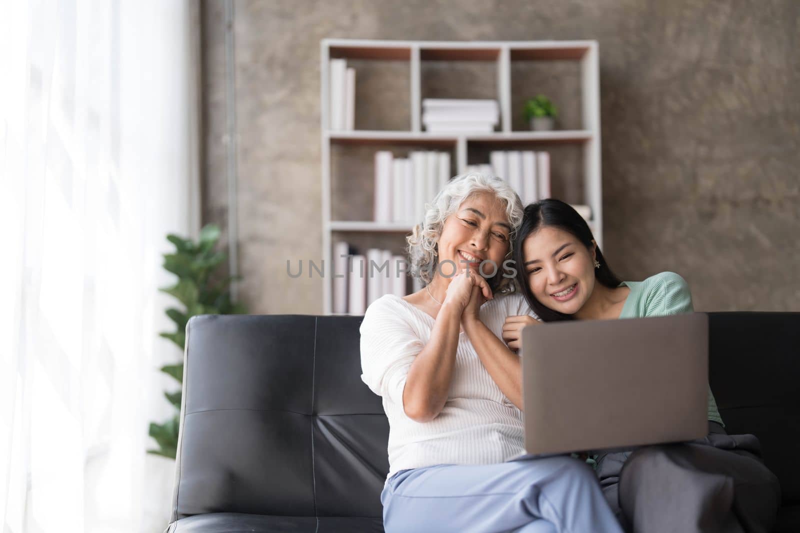 Mature mother grown up daughter sit on couch in living room hold on lap pc looking at screen watching movie film, using device make video call, shopping via e-commerce website, girl teach mom concept..