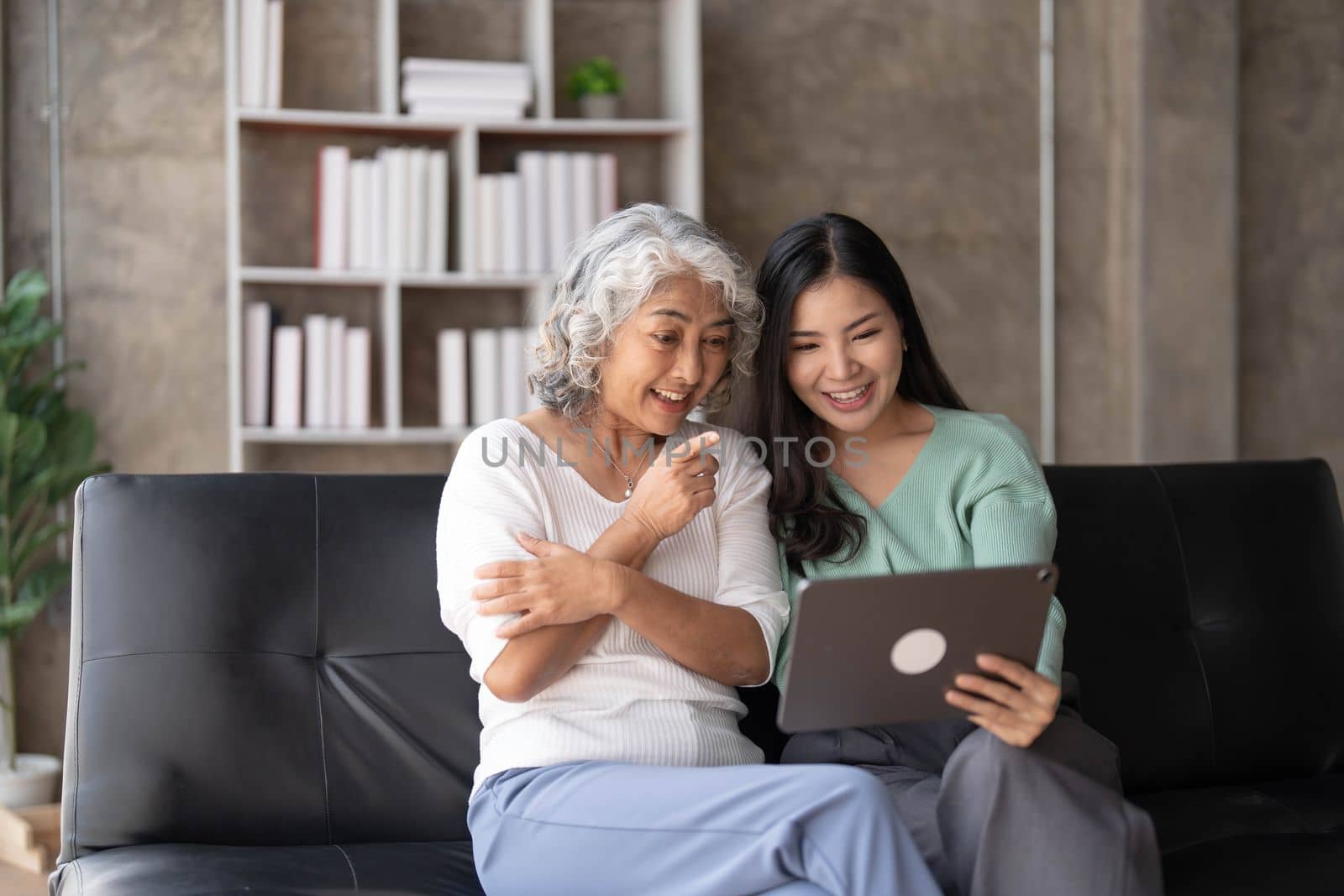 Mature mother grown up daughter sit on couch in living room hold on lap pc looking at screen watching movie film, using device make video call, shopping via e-commerce website, girl teach mom concept..