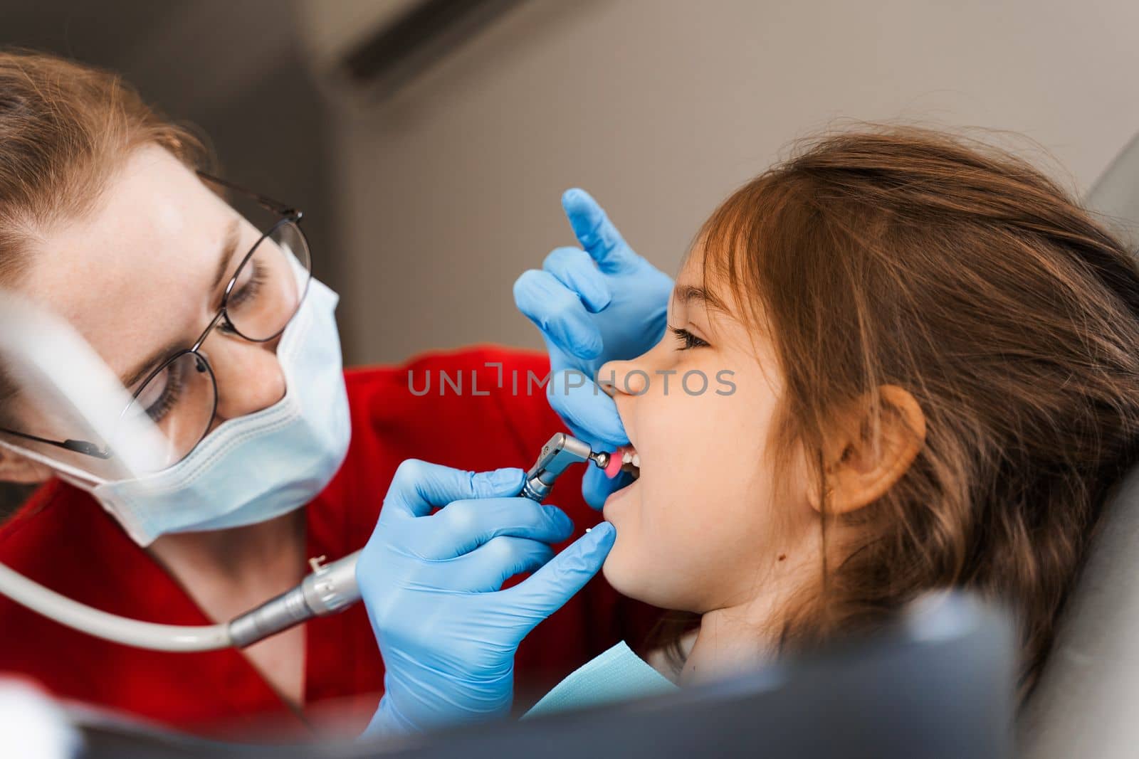 Pediatric girl dentist makes professional teeth cleaning in dentistry. Professional hygiene for teeth of child in dentistry. Pediatric dentist examines and consults kid patient in dentistry. by Rabizo