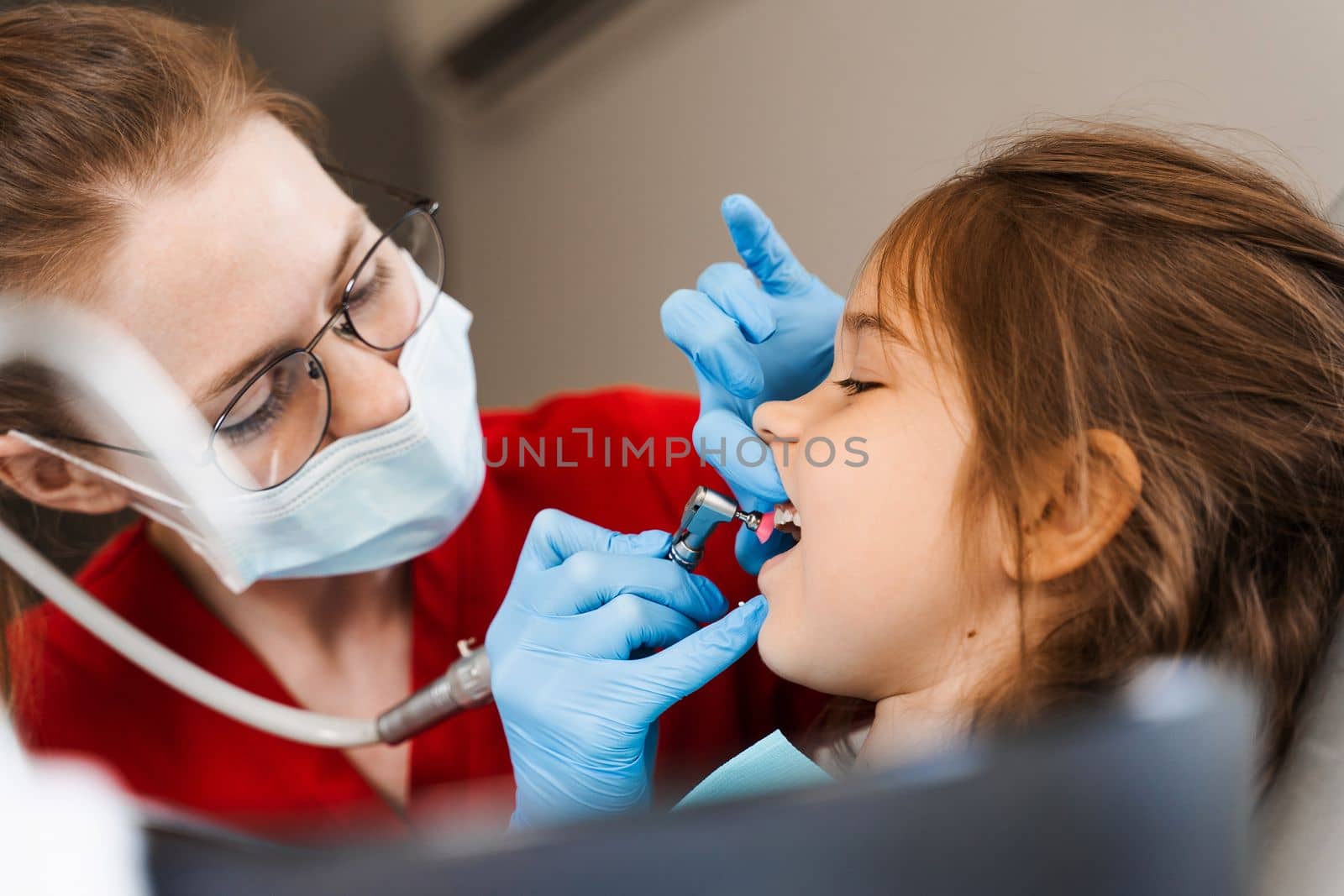 Pediatric girl dentist makes professional teeth cleaning in dentistry. Professional hygiene for teeth of child in dentistry. Pediatric dentist examines and consults kid patient in dentistry. by Rabizo