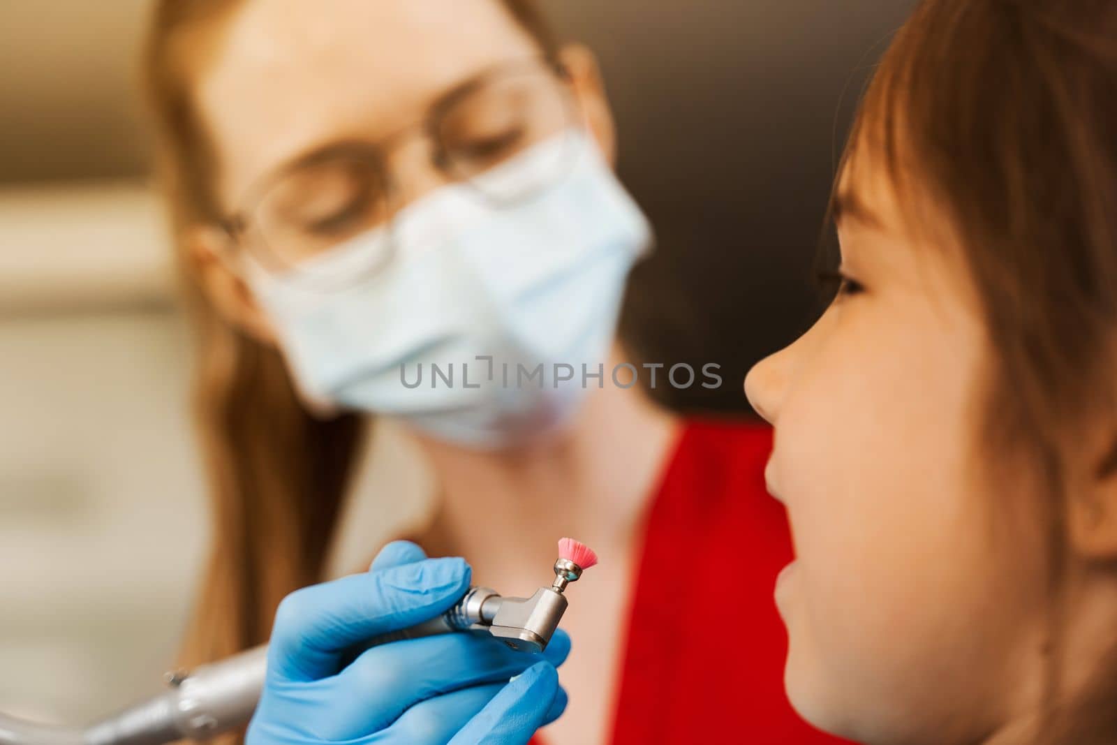 Child dentist makes professional teeth cleaning close-up in dentistry. Professional hygiene for teeth of child in dentistry. Pediatric dentist examines and consults kid patient in dentistry. by Rabizo