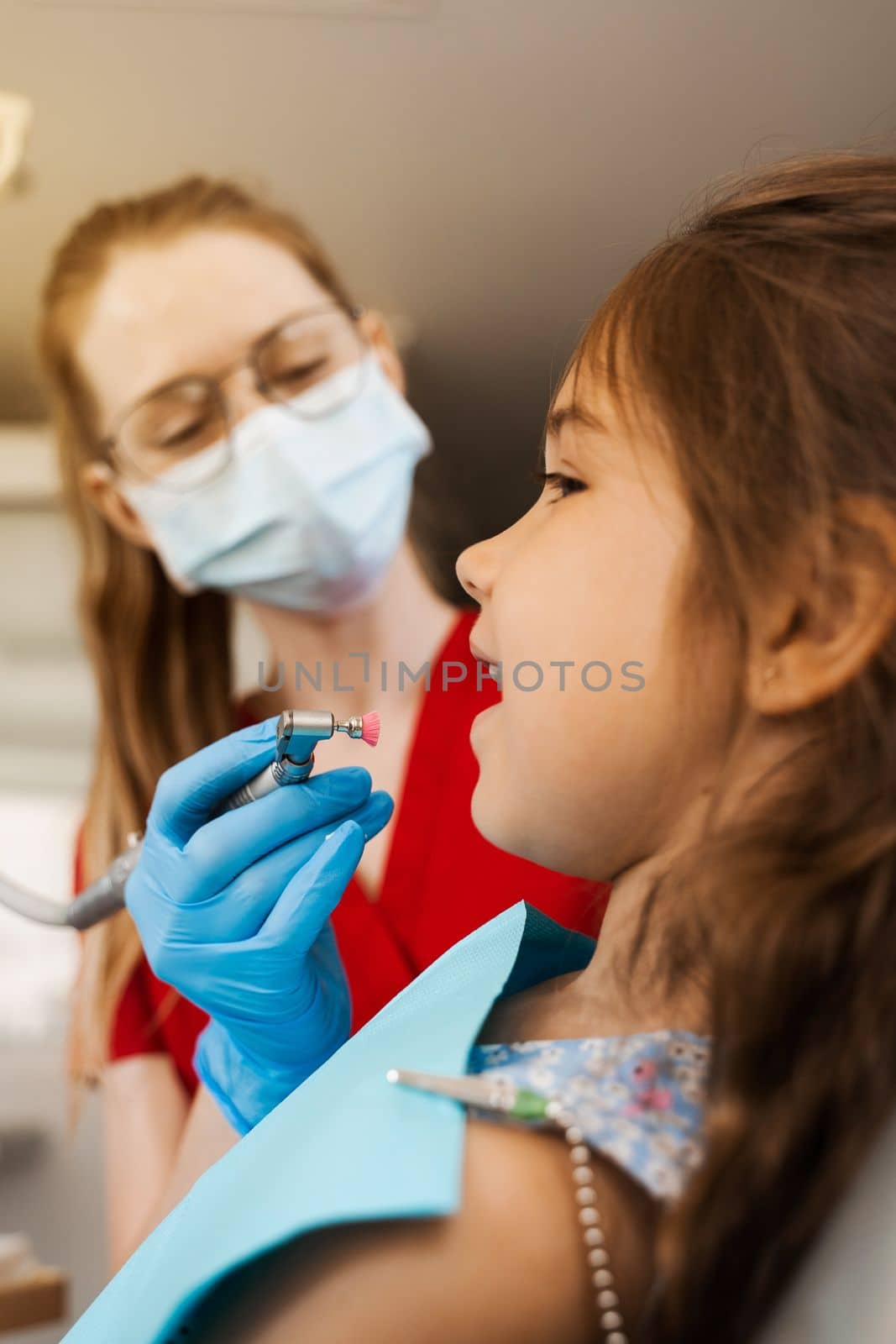 Professional teeth cleaning for child girl in dentistry. Professional hygiene for teeth of child. Pediatric dentist examines and consults kid patient in dentistry. by Rabizo