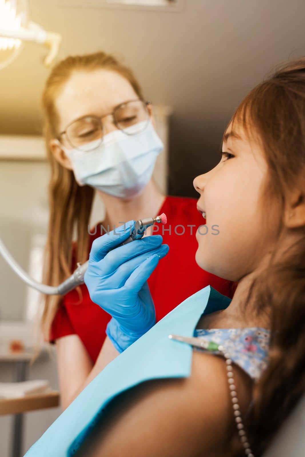 Professional teeth cleaning for child girl in dentistry. Professional hygiene for teeth of child. Pediatric dentist examines and consults kid patient in dentistry