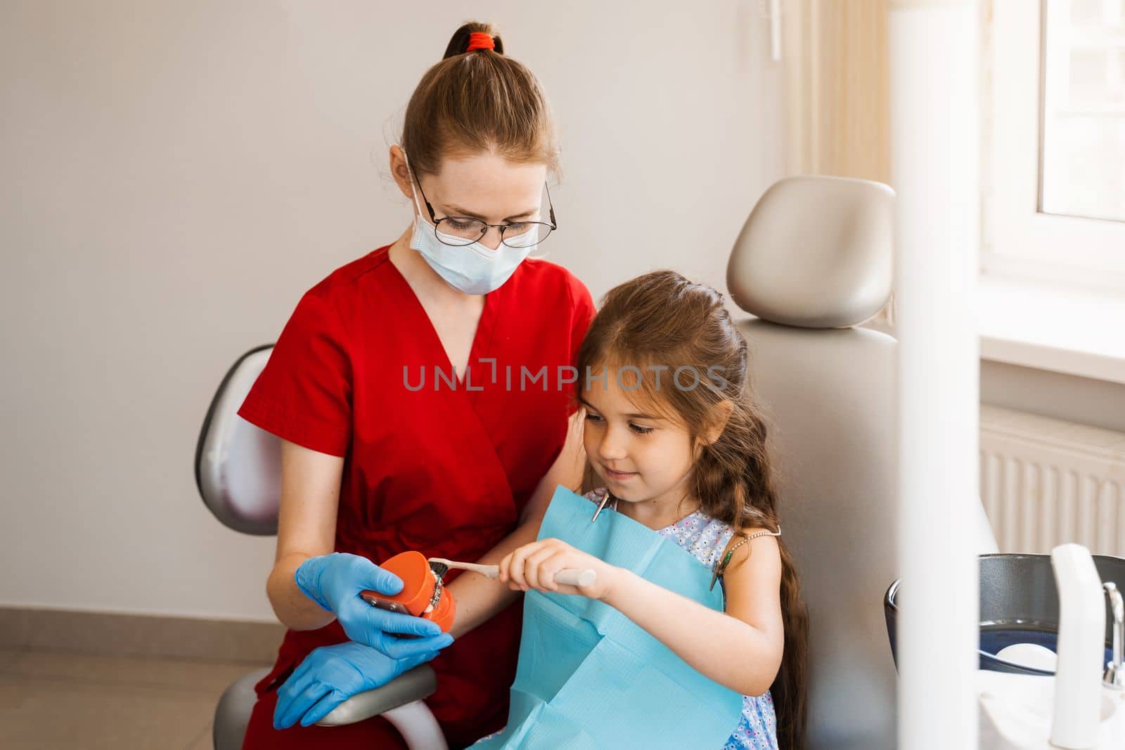 Pediatric dentist teaching oral hygiene lesson for kids in dentistry. The dentist shows child how to properly use toothbrush for brush teeth. Jaw anatomical model teeth brushing. by Rabizo