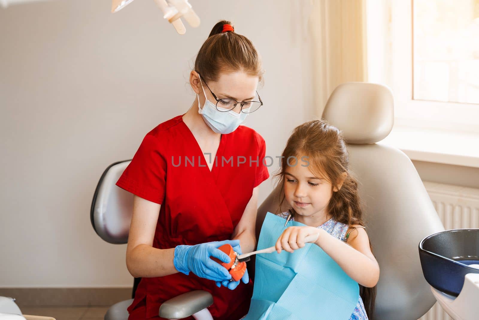 Dentist shows child how to properly use toothbrush for brush teeth. Jaw anatomical model teeth brushing. Pediatric dentist teaching oral hygiene lesson for kids in dentistry. by Rabizo
