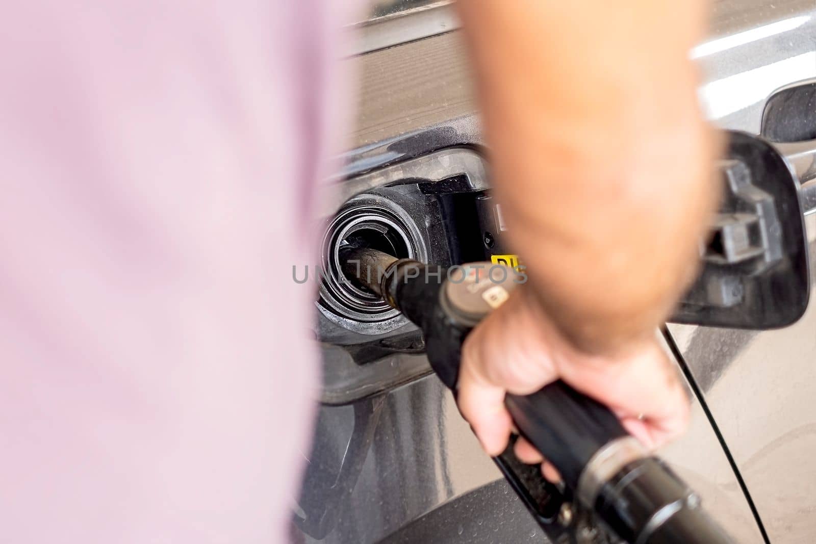 Close up of hand holding gas gun while refueling car with gasoline. Filling fuel into tank of auto at gas station.
