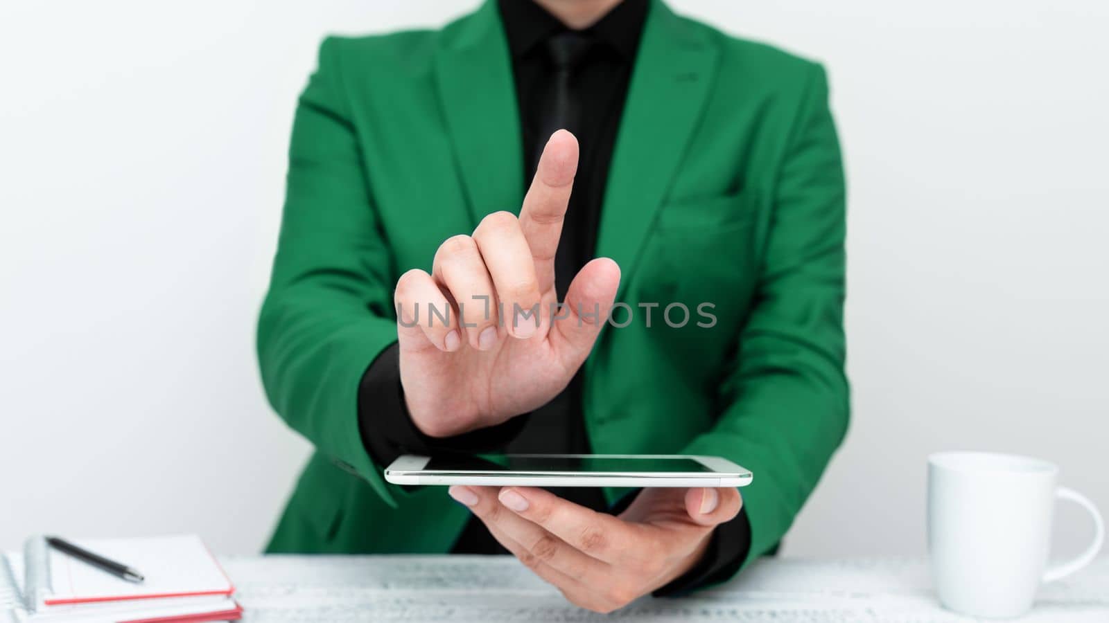 Businessman in Green jacket sitting at table holding mobile phone And Pointing With One Finger On Important Message. Gentleman Showing Critical Announcement. by nialowwa