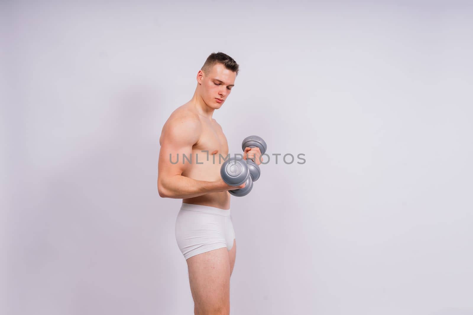 Shirtless bodybuilder holding a dumbell and showing his muscular arms.