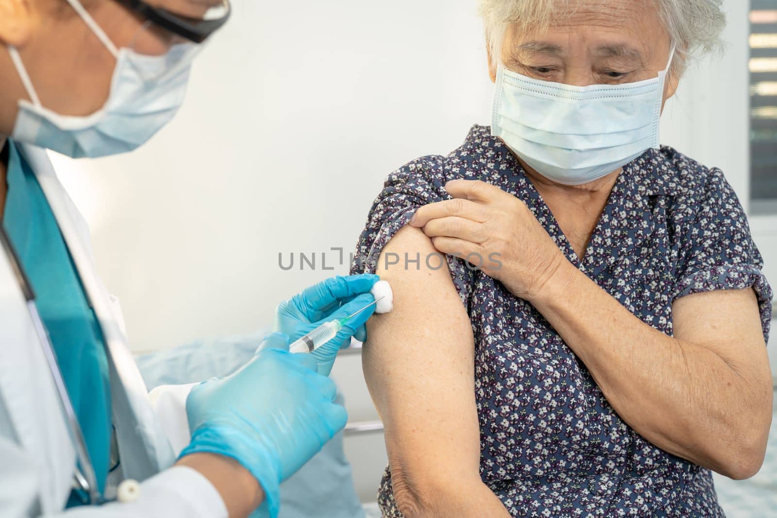 Elderly Asian senior woman wearing face mask getting covid19 or coronavirus vaccine by doctor make injection. by pamai