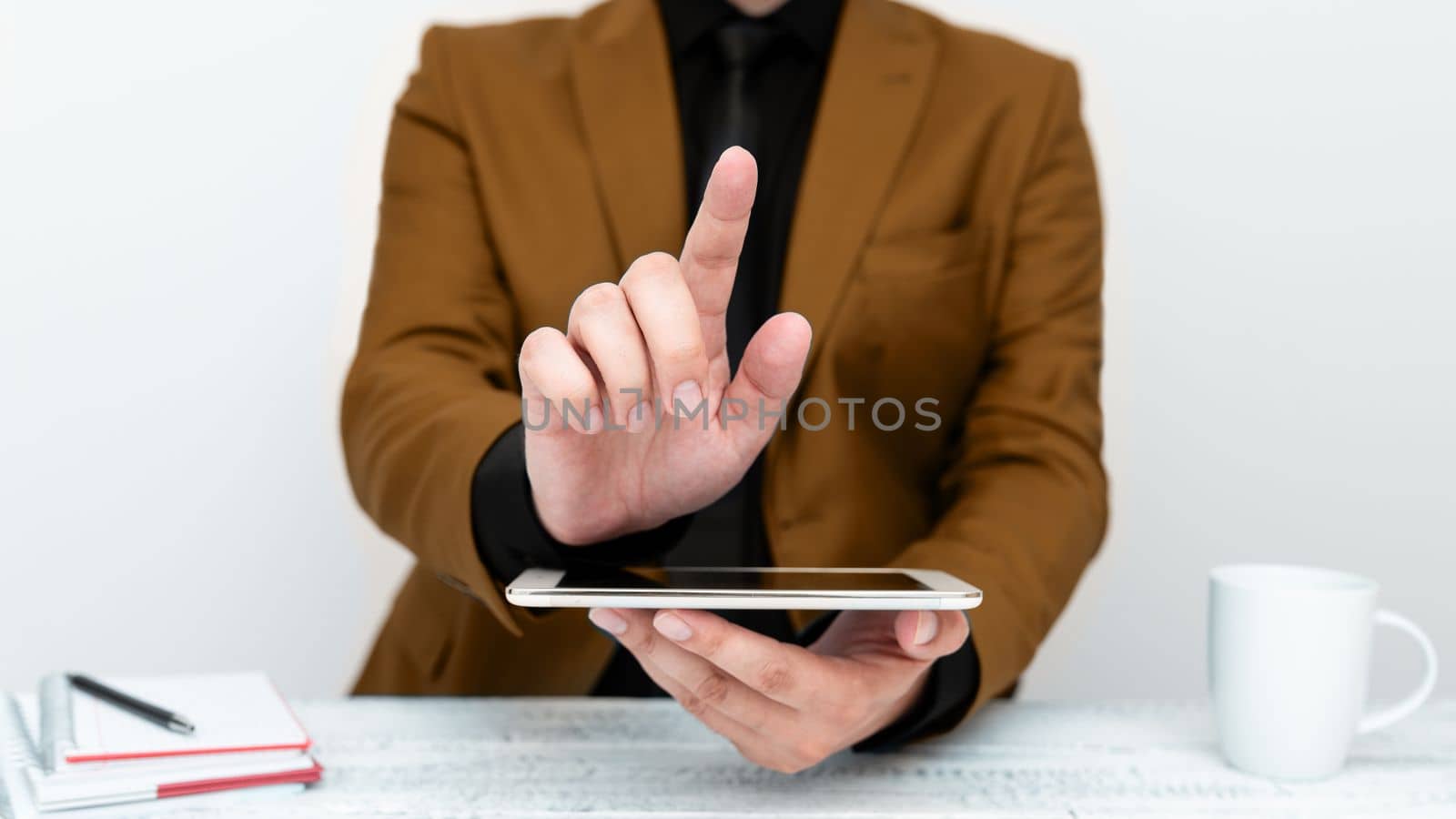 Businessman in Brown jacket sitting at table holding mobile phone And Pointing With One Finger On Important Message. Gentleman Showing Critical Announcement. by nialowwa