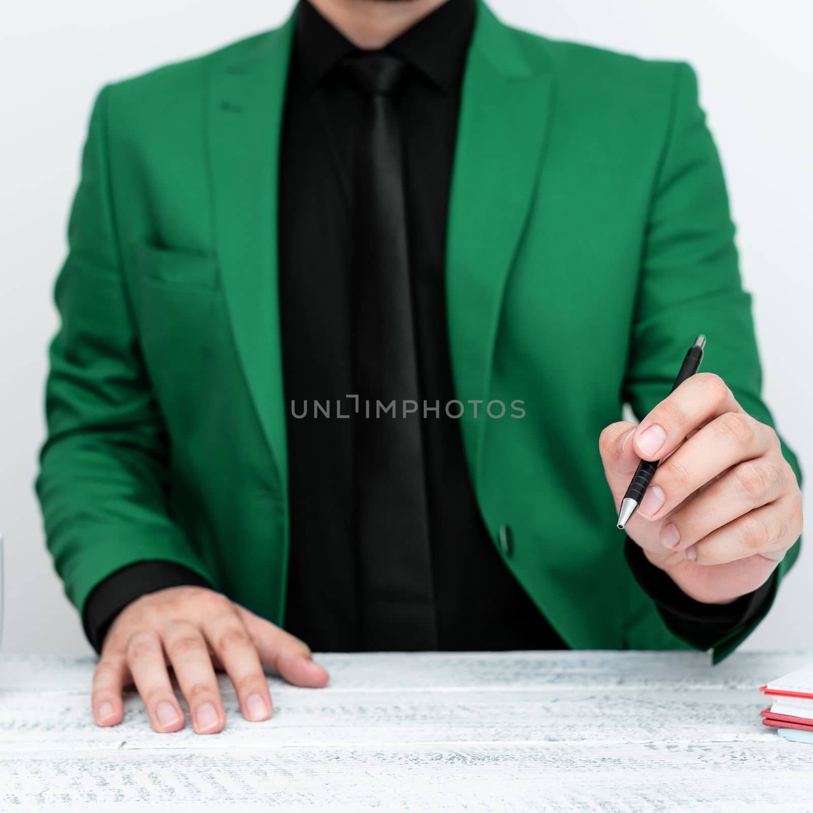 Male model in Green suit sitting at white table And Pointing With Pen On Important Message. Gentleman Showing Critical Announcement. Coffee cup on deck. by nialowwa
