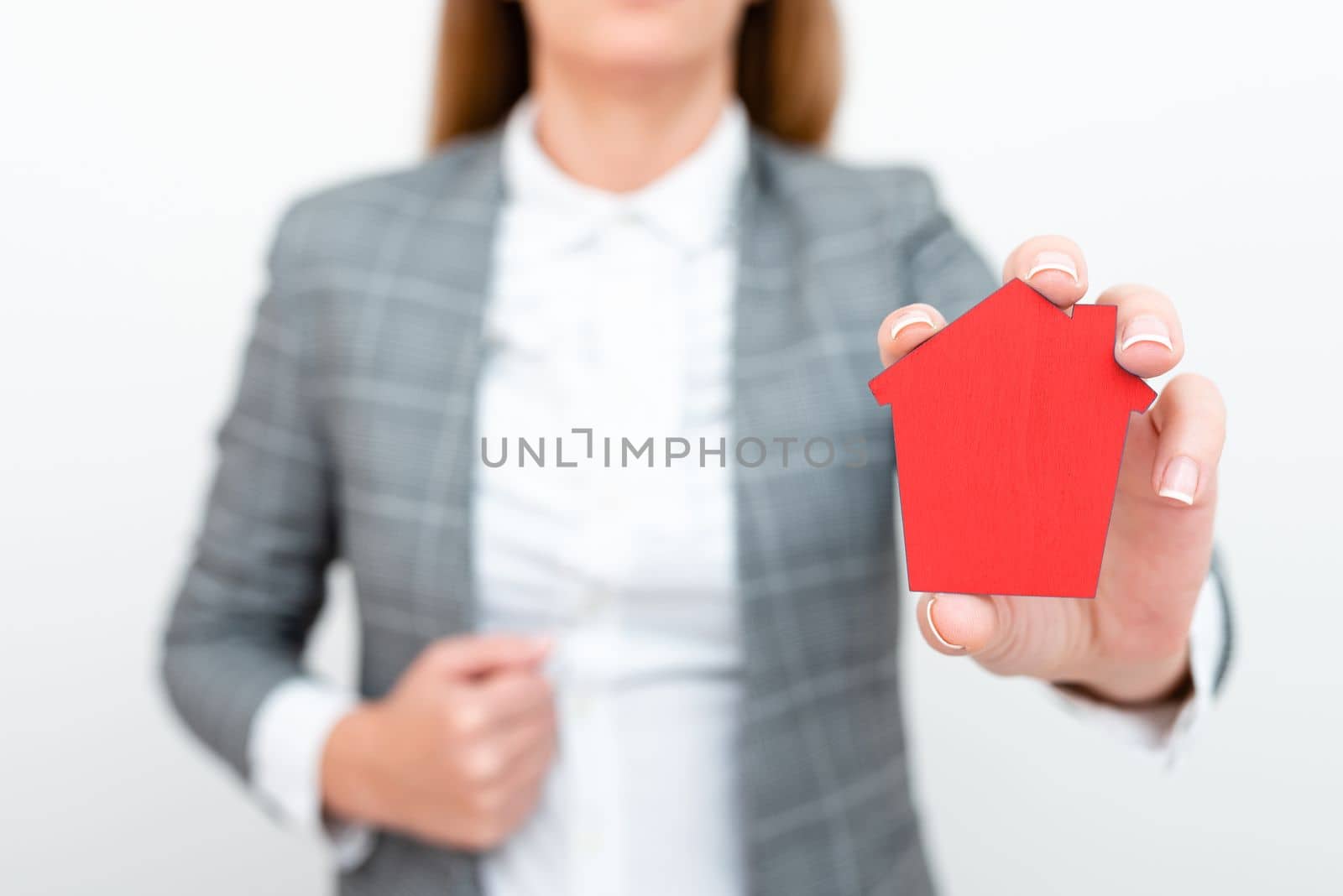 Businesswoman in gray suit holding colored paper house in one hand. Showing Important Informations. Executive Displaying Late News. Woman Showing Recent Updates. by nialowwa