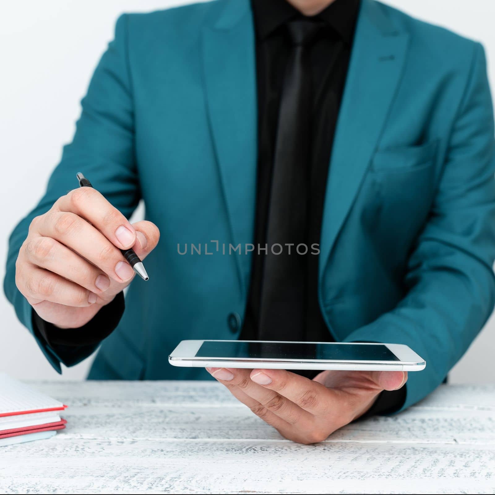 Man in Blue jacket sitting at white table And Pointing With Pen On Important Message. Holding mobile phone. Gentleman Showing Critical Announcement. by nialowwa