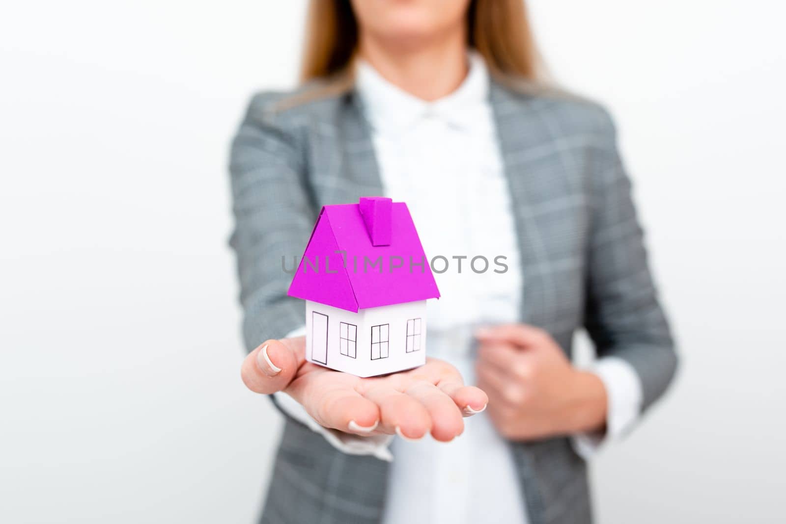 Businesswoman in a gray suit holding a colored paper house in one hand.