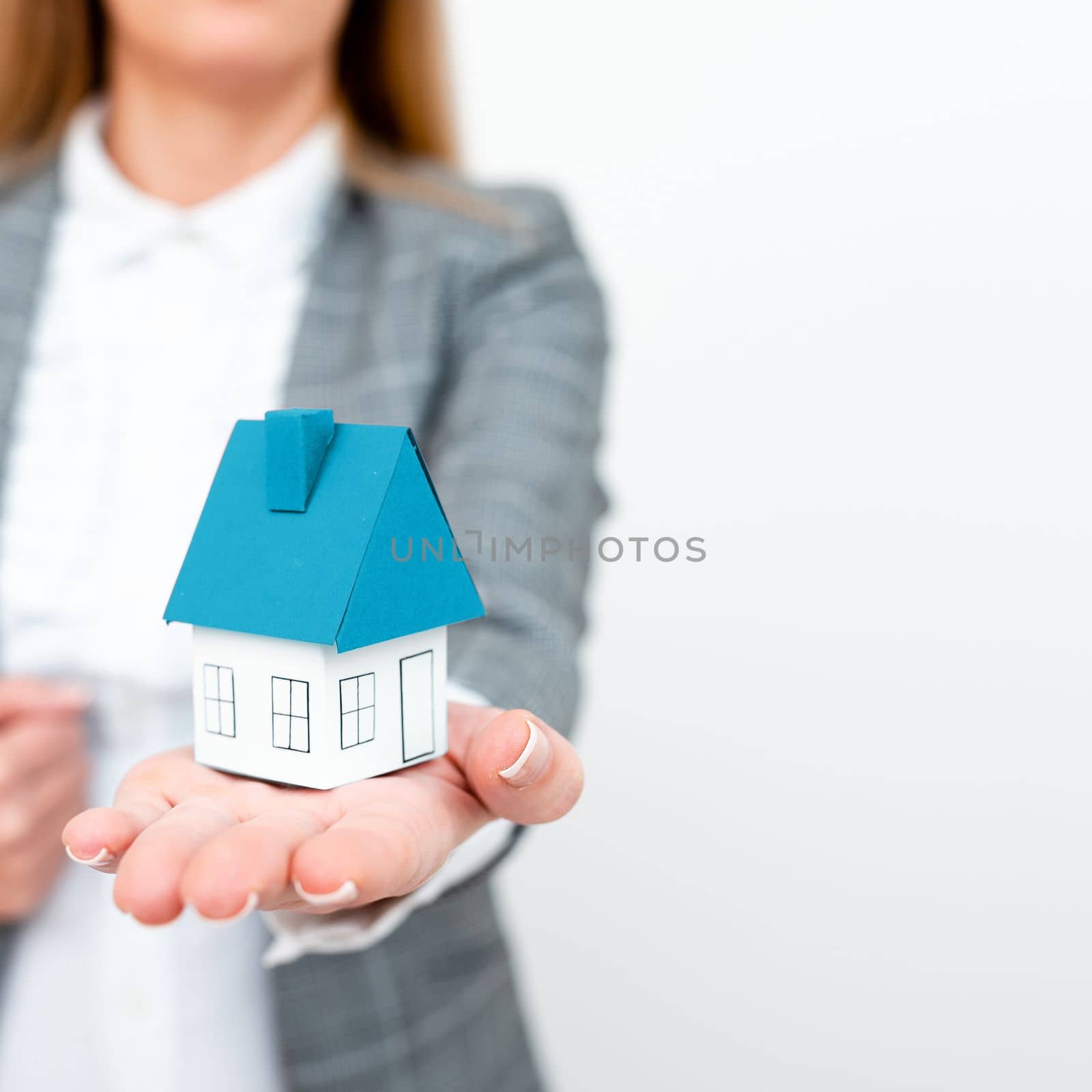 Businesswoman in gray suit holding colored paper house in one hand. Showing Important Informations. Executive Displaying Late News. Woman Showing Recent Updates. by nialowwa